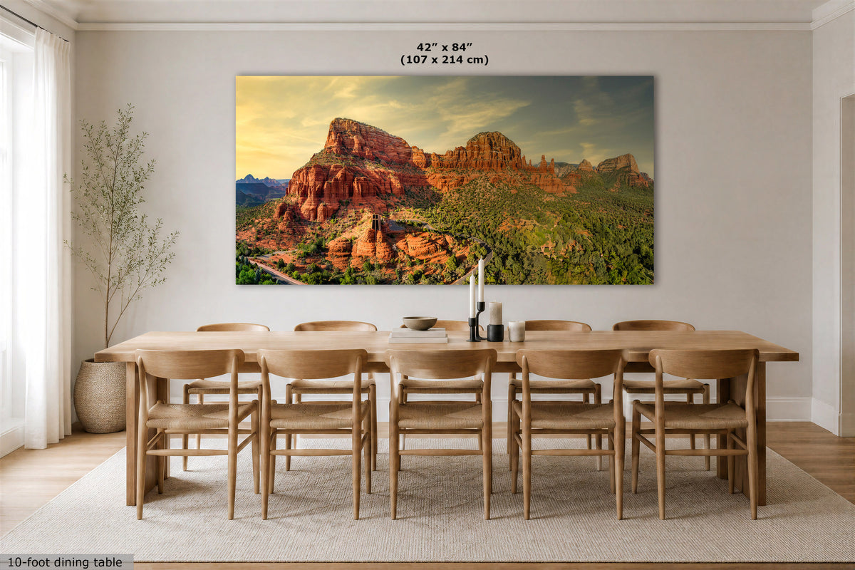 A large rectangular wall art print showing a desert canyon landscape with red rock formations and green vegetation, displayed above a wooden dining table in a bright dining room. The print includes size text at the top reading 42" x 84" (107 x 214 cm).