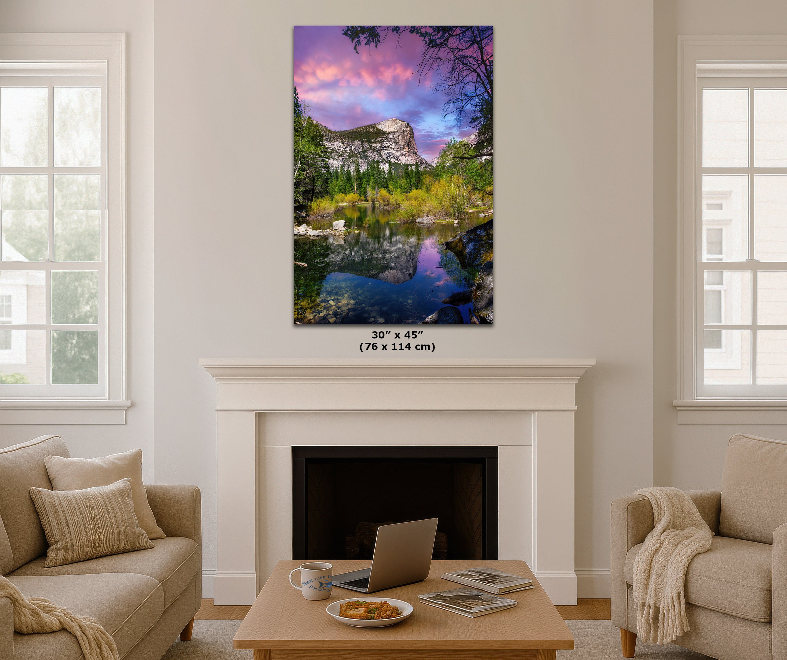 A vertical canvas wall art print depicting a colorful mountain lake landscape with pink and purple sky reflections, displayed above a white fireplace in a modern living room setting. The dimensions '30" x 45" (76 x 114 cm)' are printed below the canvas.