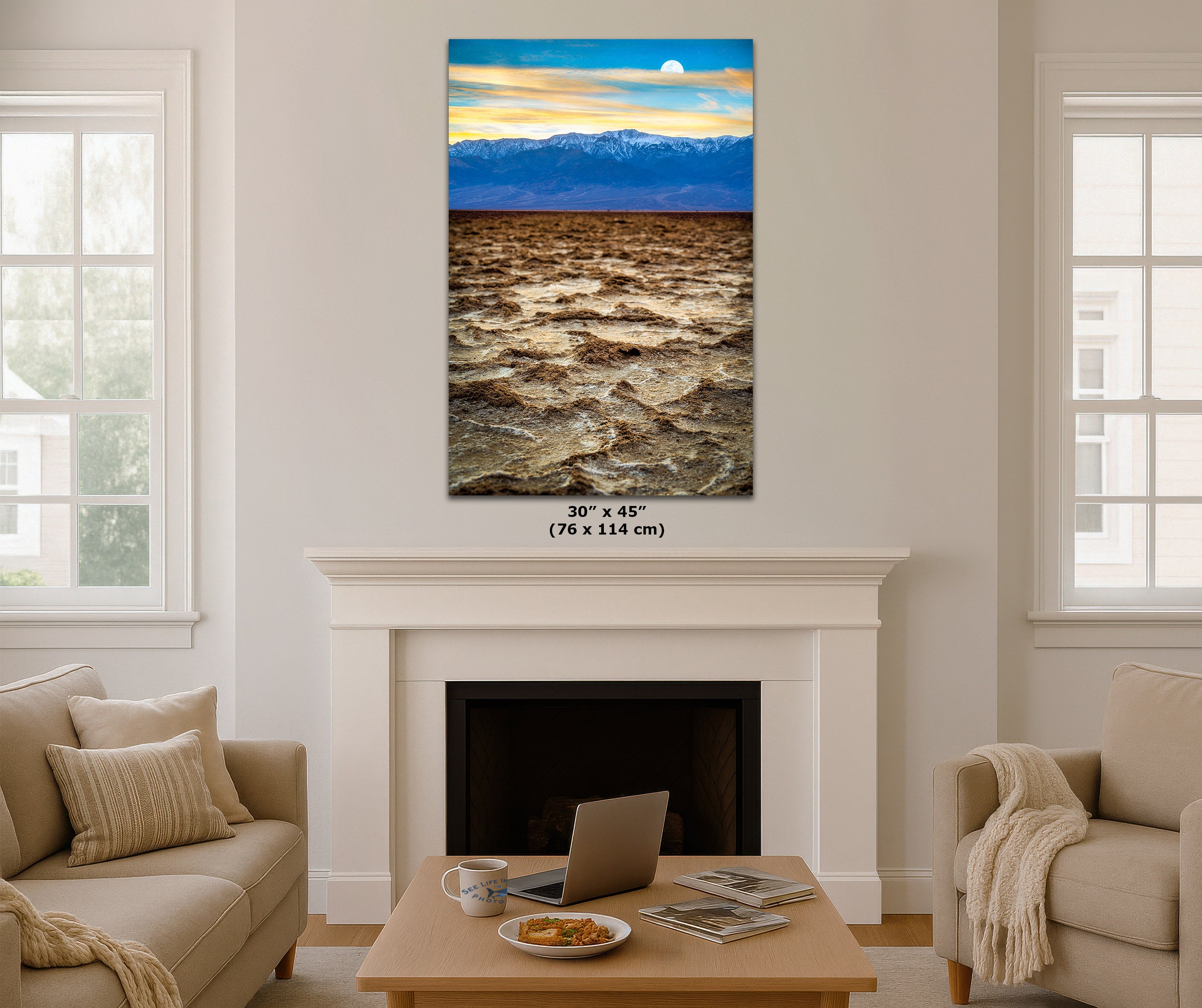 A vertical canvas wall art print depicting a landscape with a blue mountain range and a golden sky, displayed above a white fireplace mantel in a modern living room setting. The print features a size dimension overlay of 30" x 45" (76 x 114 cm).