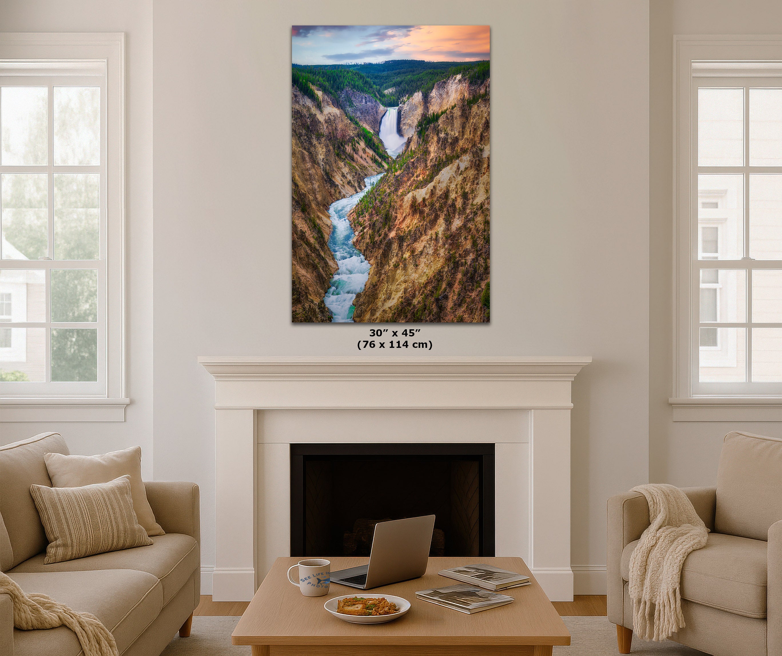 A vertical canvas print of a scenic canyon with a waterfall and river, displayed on a white fireplace mantel in a modern living room setting. The print features a sunset sky and has size text overlay below it.