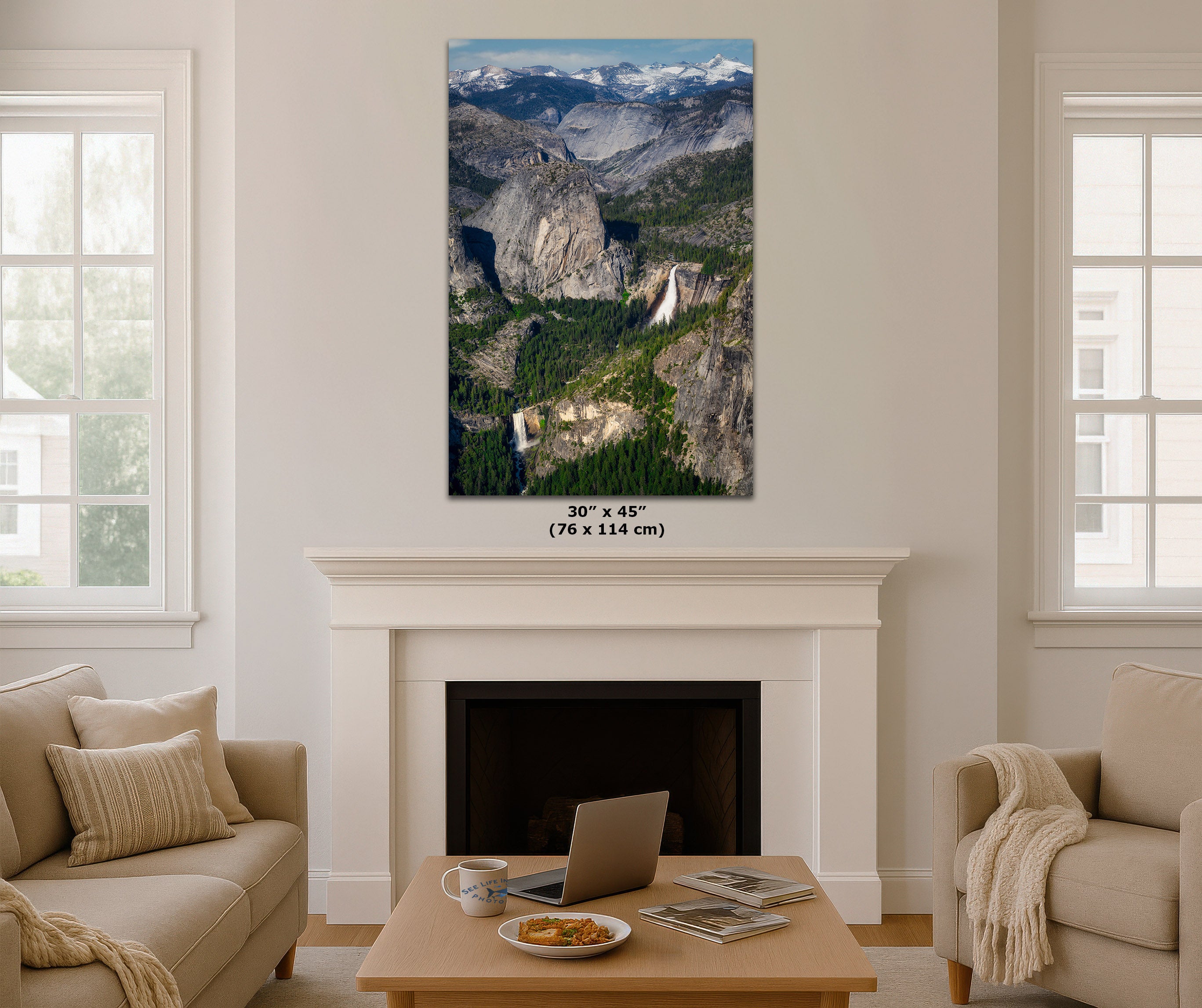 A vertical canvas print of Yosemite Valley with mountains, forests, and waterfalls, displayed on a white fireplace mantel in a modern living room setting. The dimensions '30" x 45" (76 x 114 cm)' are printed below the canvas.