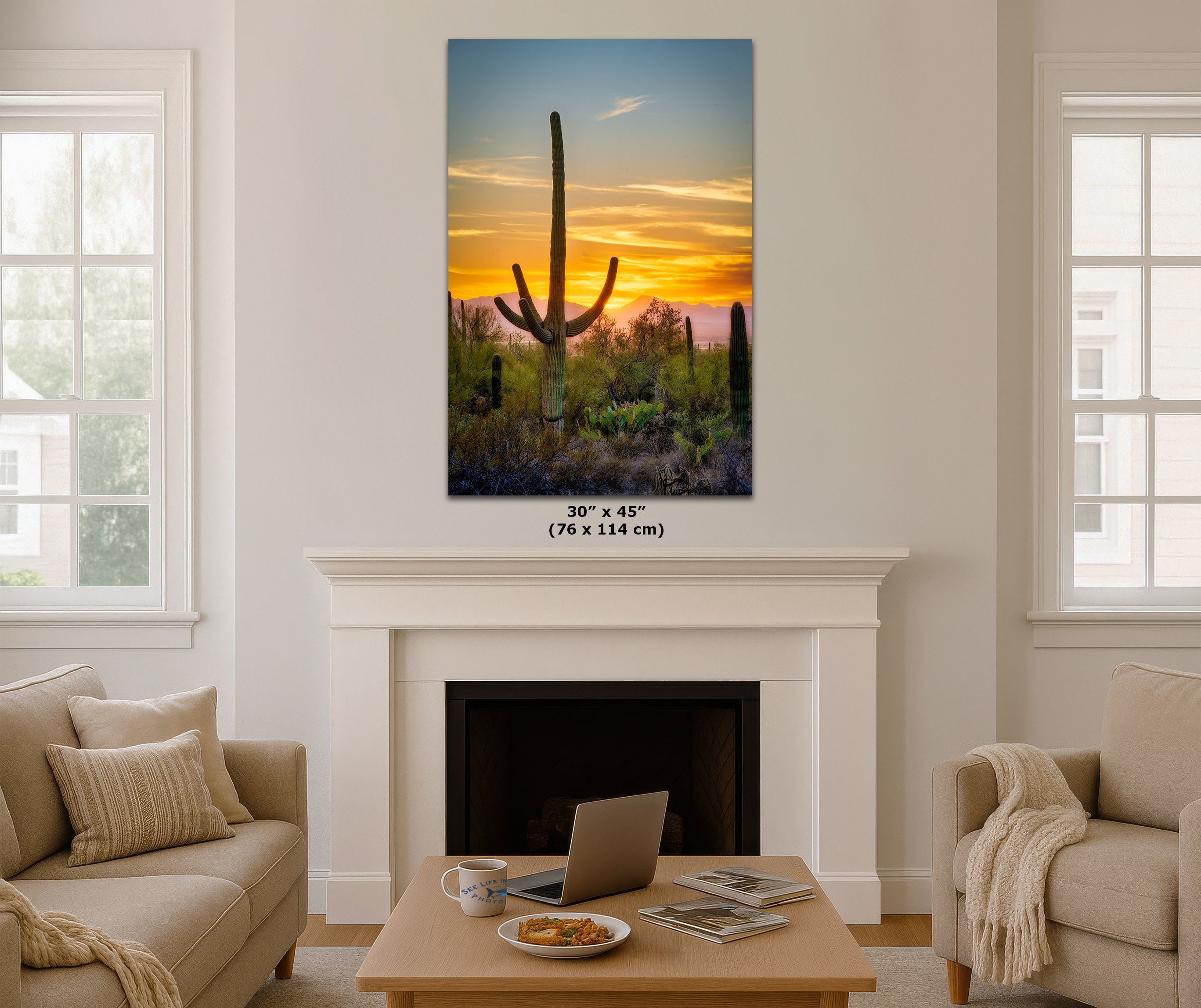 A 30 x 45 inch canvas print of a desert sunset with a saguaro cactus, displayed on a white wall above a fireplace in a modern living room setting.