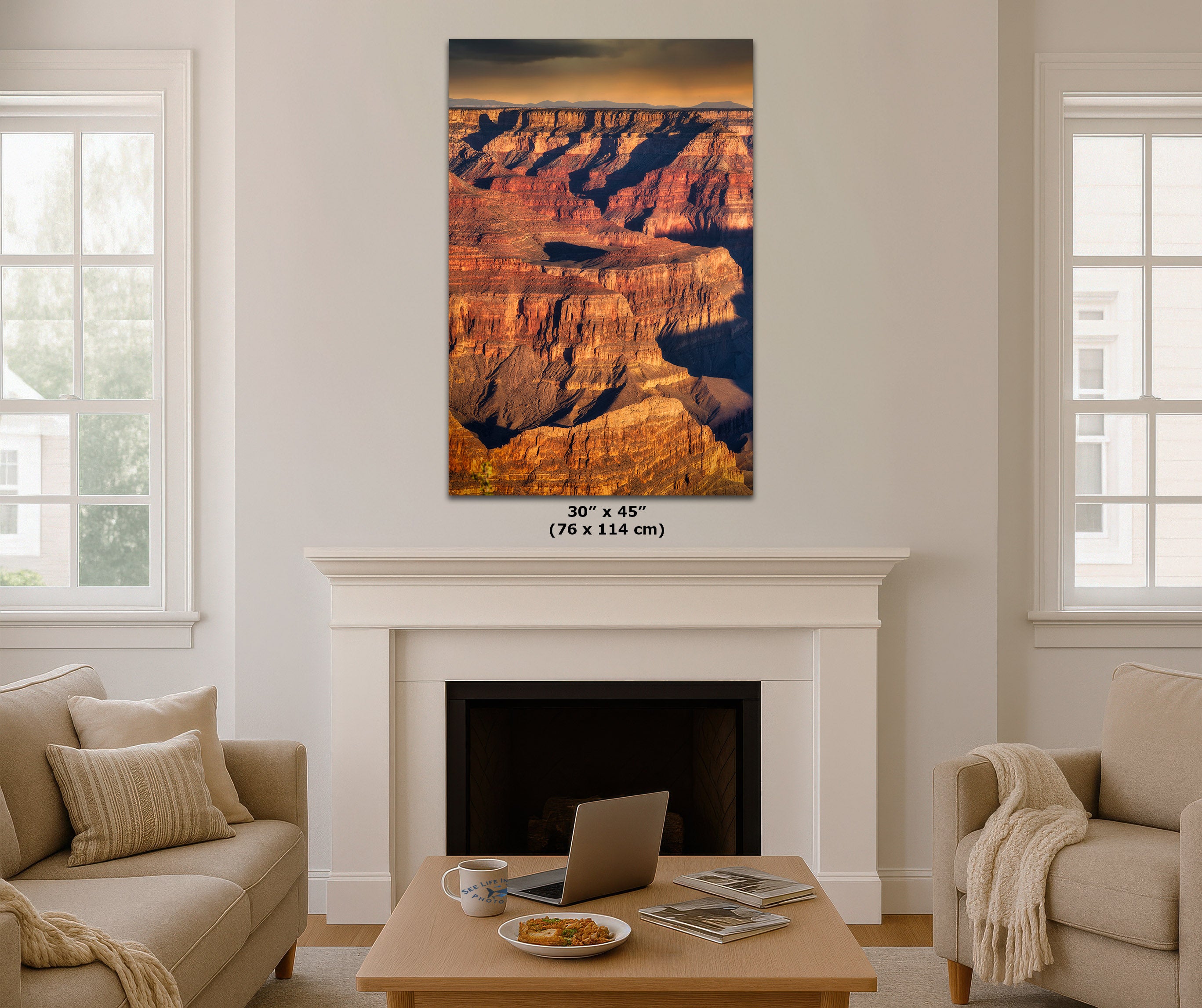 A vertical canvas wall art print depicting the Grand Canyon, displayed in a mockup living room setting above a white fireplace mantel. The print features warm sunset hues of orange, red, and brown canyon rock formations.