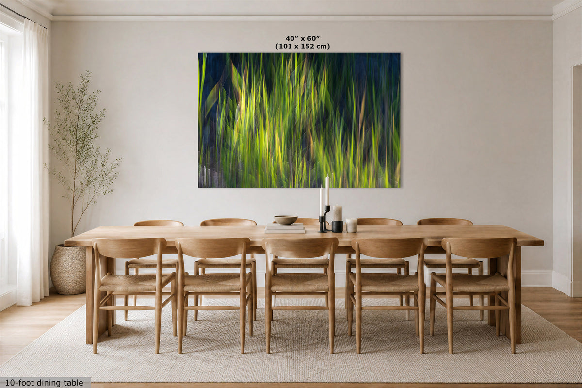 A large abstract canvas print featuring vibrant green and yellow brushstrokes on a dark blue background, displayed on a beige wall above a wooden dining table and chairs in a modern dining room.