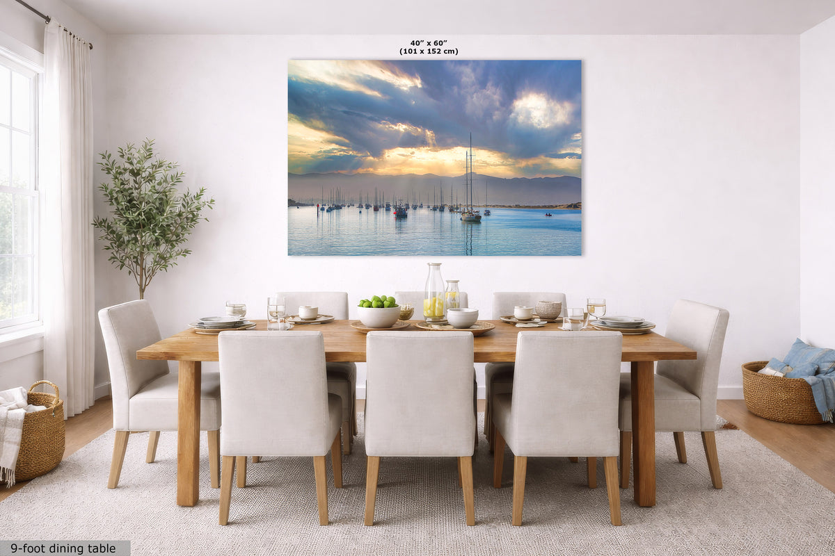 A large rectangular wall art print showing a calm harbor scene with sailboats at sunset, displayed above a wooden dining table and chairs in a bright dining room. Small text at the top reads 40 x 60 inches, and text at the bottom left says 9-foot dining table.