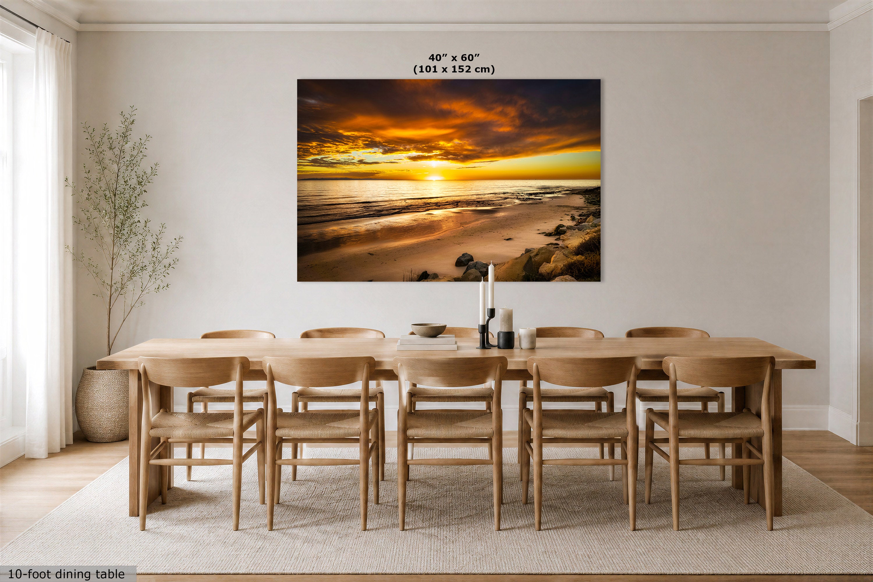A large rectangular wall art print showing a dramatic beach sunset, displayed above a wooden dining table and chairs in a bright modern dining room. The print includes size text at the top reading 40" x 60" (101 x 152 cm).