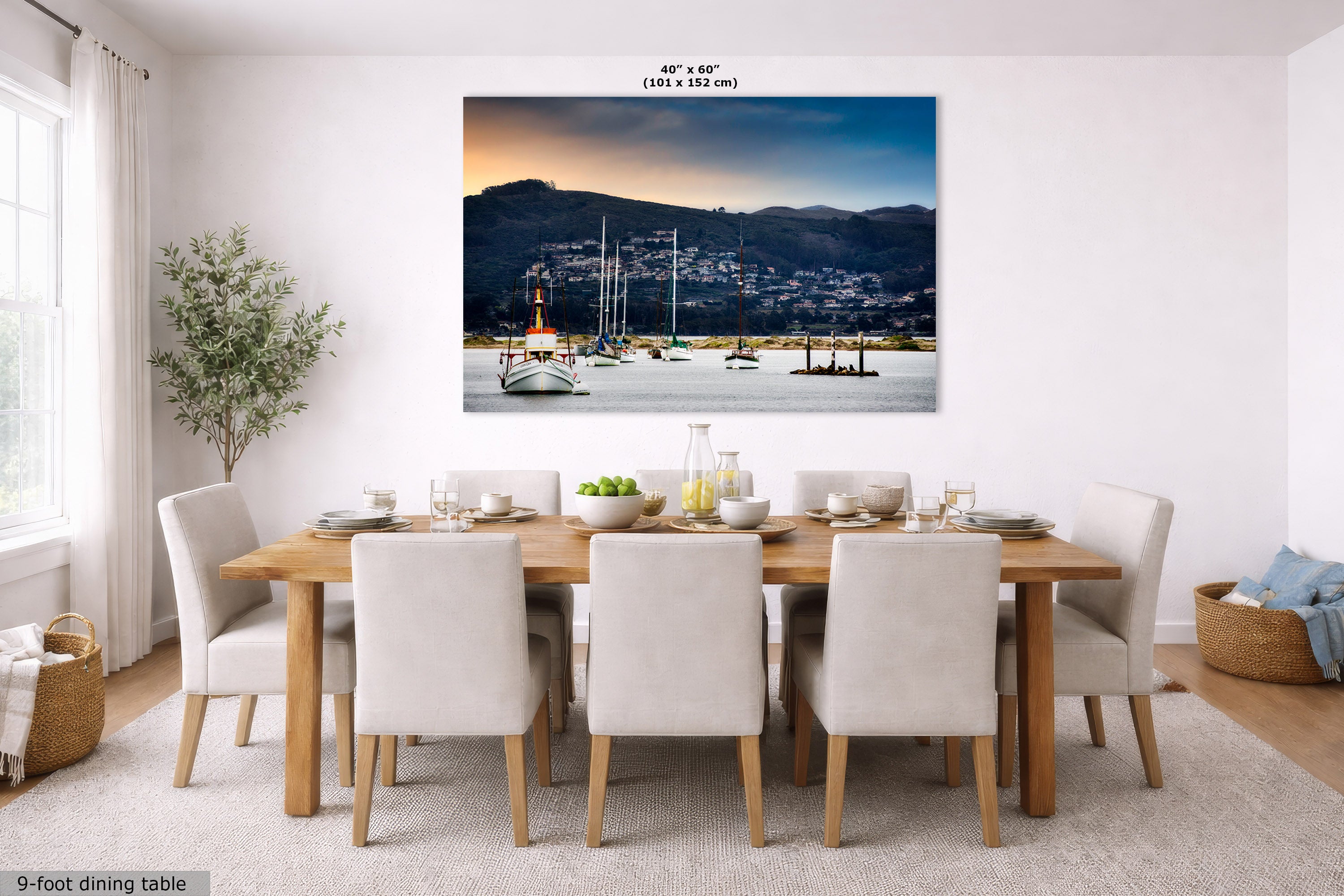 A large rectangular wall art print showing a harbor scene with boats, hills, and a sunset sky, displayed above a dining table in a bright modern room. The print includes size text at the top reading 40 x 60 inches (101 x 152 cm).
