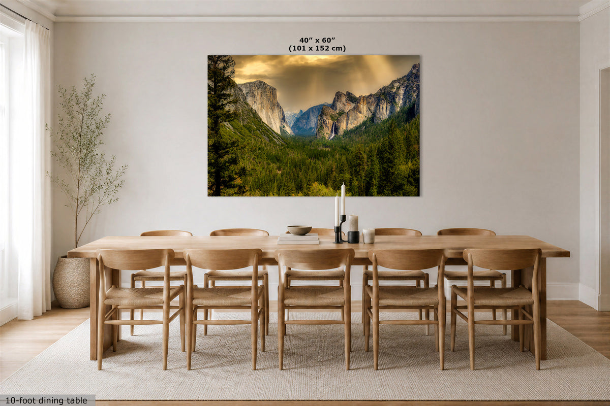 A large wall art print showing a mountain valley landscape with green trees and dramatic clouds, displayed above a wooden dining table and chairs in a bright neutral dining room. Text at the top reads 40" x 60" (101 x 152 cm), and a small caption at the bottom left says 10-foot dining table.