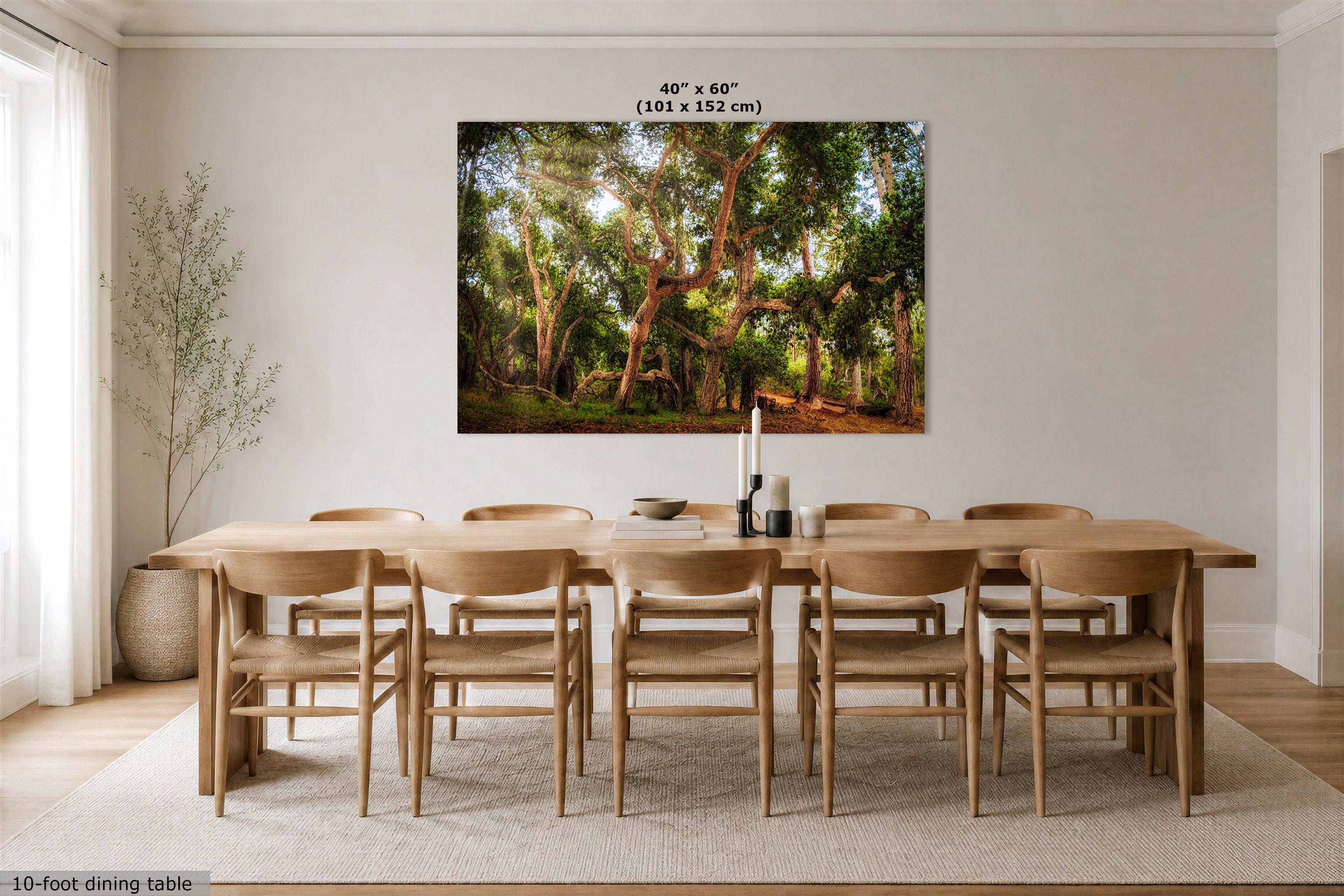 A large framed wall art print showing a sunlit forest scene with trees and green foliage, displayed above a wooden dining table and chairs in a bright neutral dining room. Text at the top reads 40" x 60" (101 x 152 cm), and text at the bottom left says 10-foot dining table.