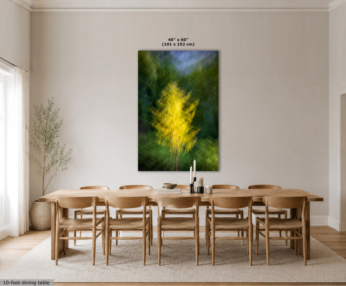 A large vertical wall art print showing a bright yellow tree in a green forest, displayed above a wooden dining table and chairs in a modern dining room. The print includes size text at the top and a small text label in the bottom left corner.