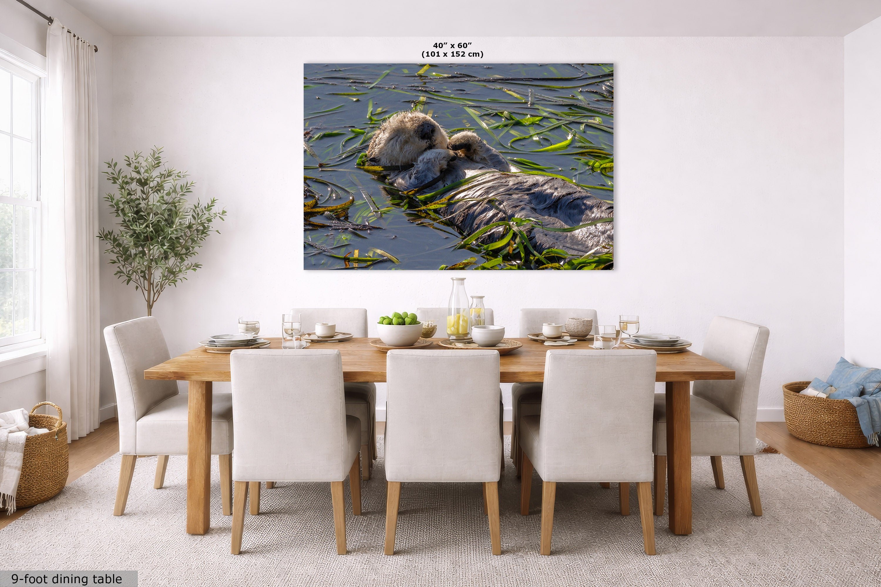 A wall art print showing a sea otter floating in water with green reeds, displayed above a wooden dining table with white chairs in a bright dining room. Small text at the top of the print reads 40 in x 60 in.