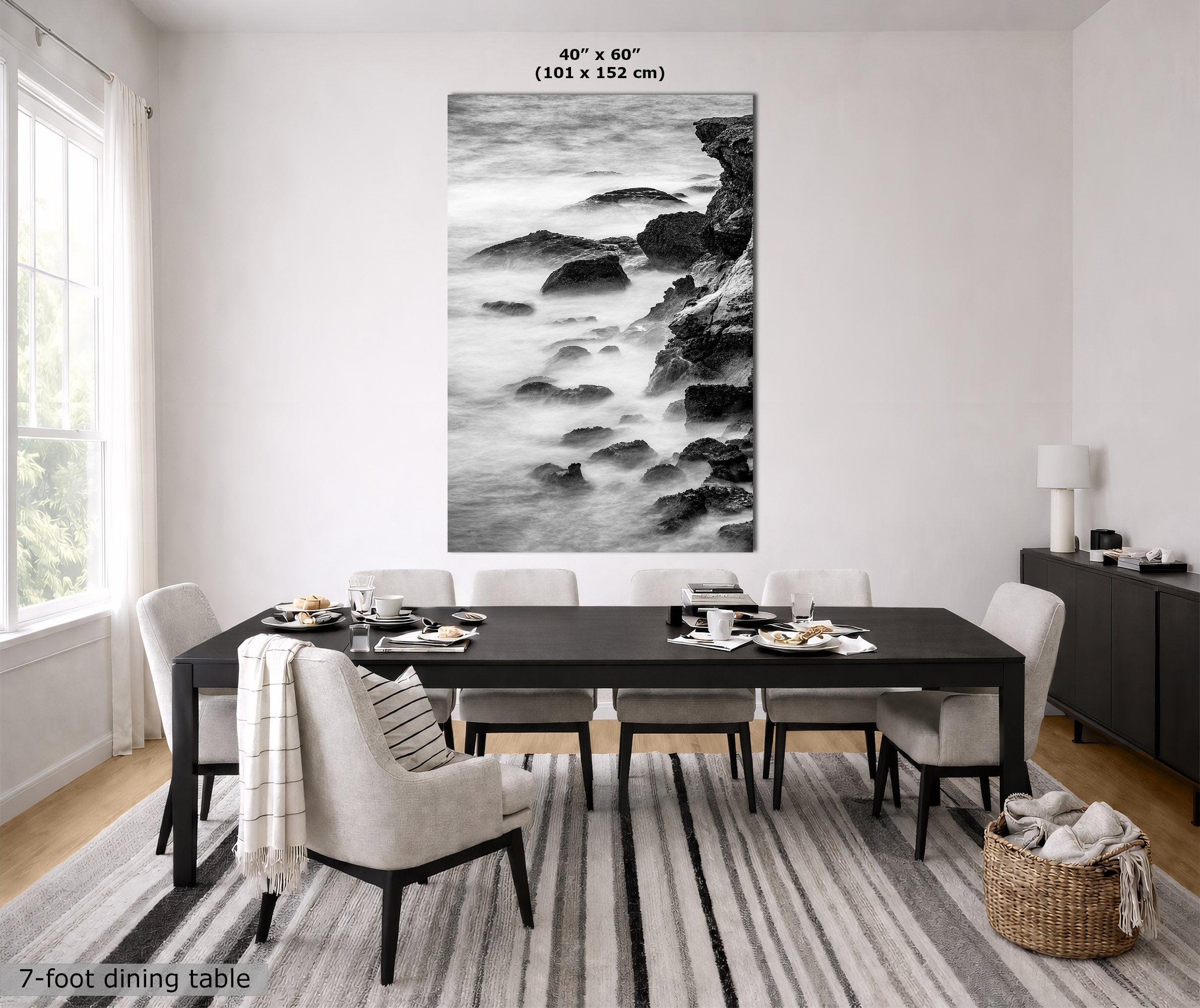 A large black and white coastal rock wall art print hangs above a dark dining table in a bright, modern dining room. The print is labeled with dimensions 40" x 60" (101 x 152 cm), and the room scene includes a dining table, chairs, rug, and sideboard.