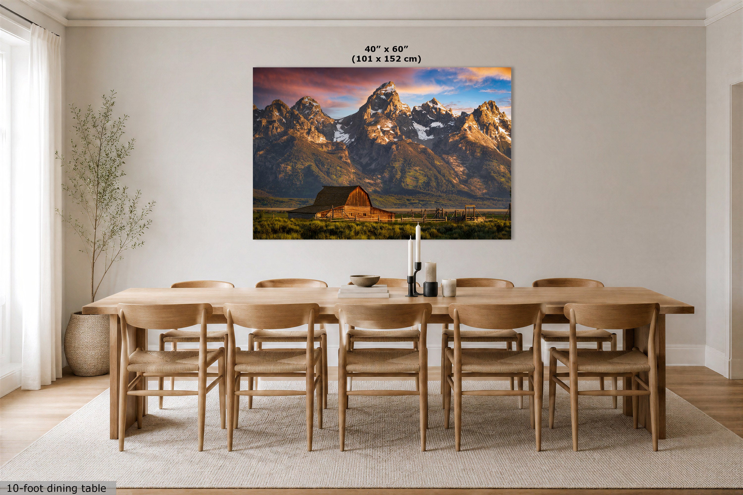 A large rectangular wall art print showing the Grand Teton mountain landscape with the Moulton Barn in the foreground, displayed above a wooden dining table and chairs in a bright dining room. The print includes the text '40" x 60" (101 x 152 cm)' at the top.