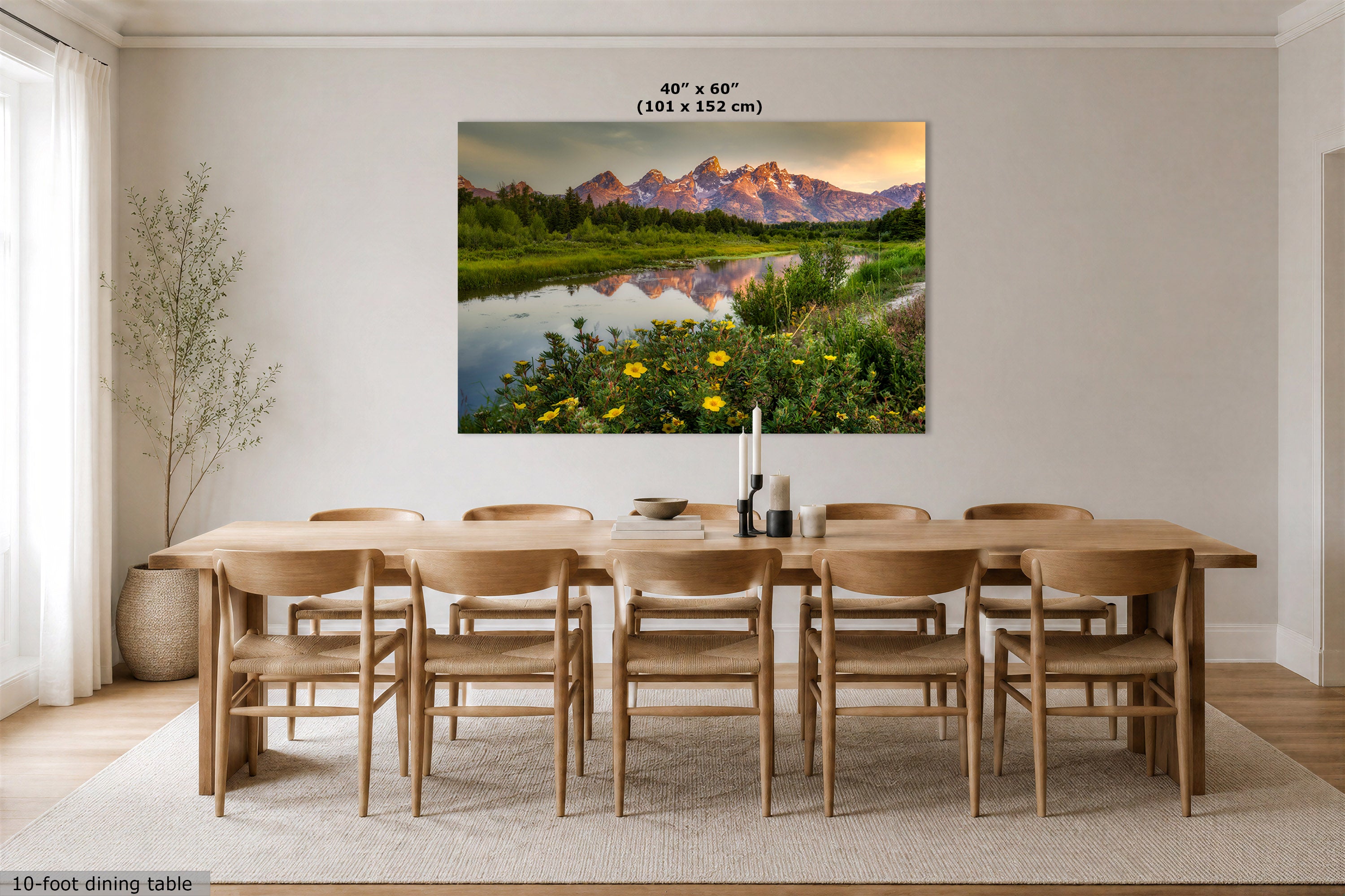 A 40" x 60" canvas print of a mountain landscape with a lake reflection hangs on a wall above a 10-foot dining table and chairs in a modern dining room.