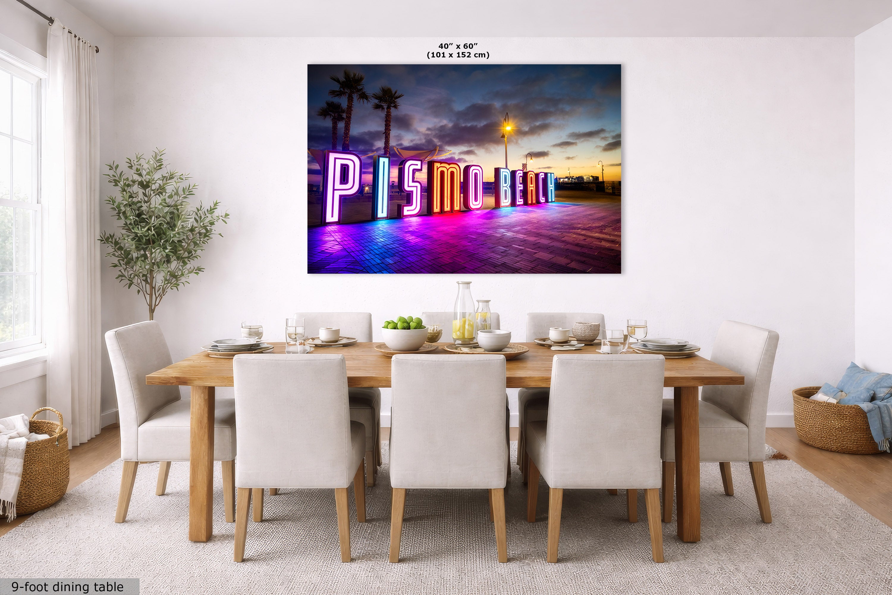 A large wall art print showing a colorful neon 'Pismo Beach' sign at sunset, displayed above a dining table in a bright, modern dining room. The print is labeled with dimensions 40" x 60" (101 x 152 cm) at the top.