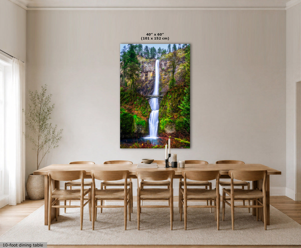 A vertical canvas wall art print depicting a lush green forest waterfall, styled in a modern dining room setting above a wooden dining table and chairs. The image includes size and dimension text overlays.