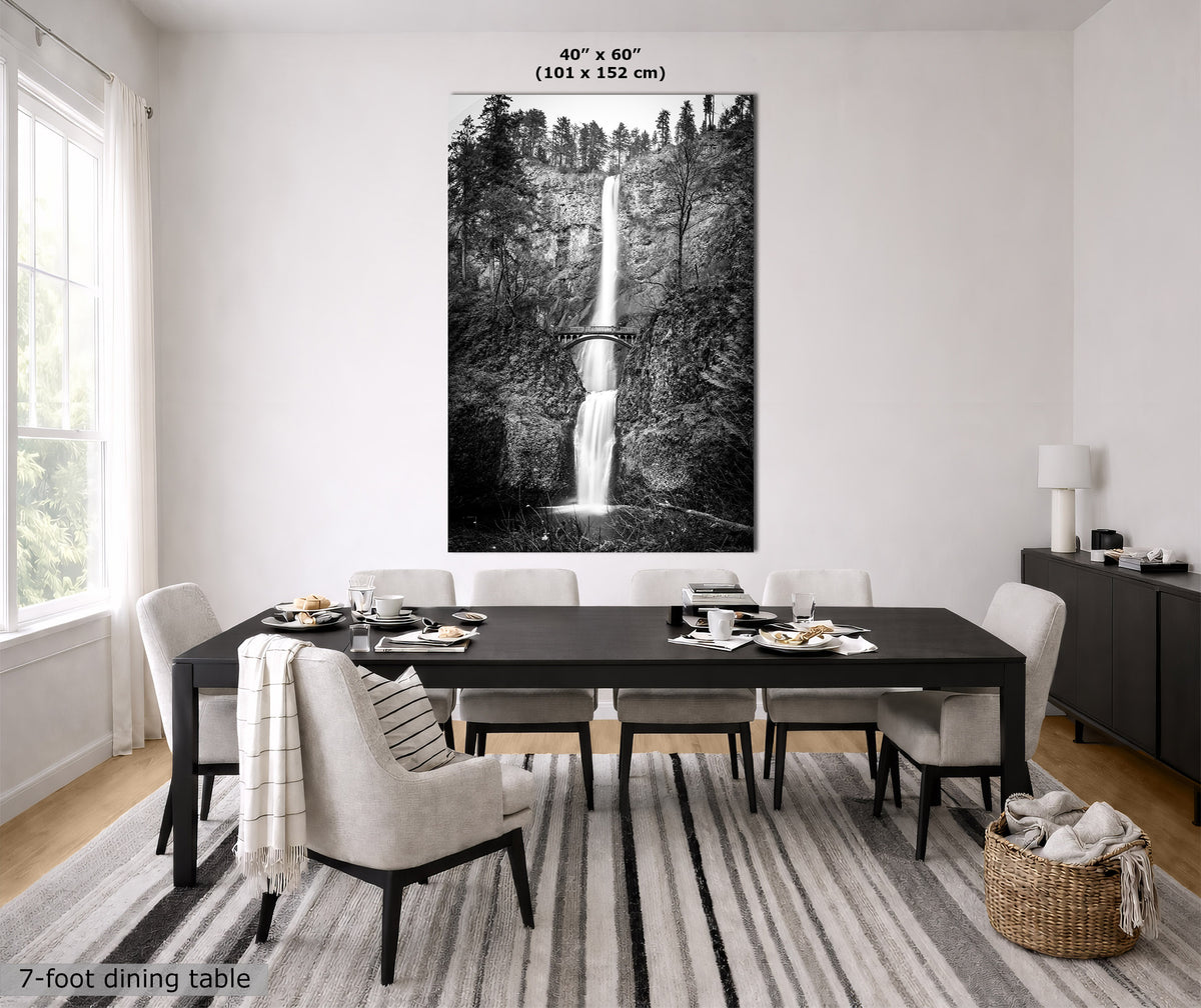 A large black and white vertical wall art print depicting a waterfall over a rocky cliff, displayed above a dark wood dining table in a bright, modern dining room. Text on the image indicates the print size is 40" x 60" (101 x 152 cm) and the dining table is 7-foot.