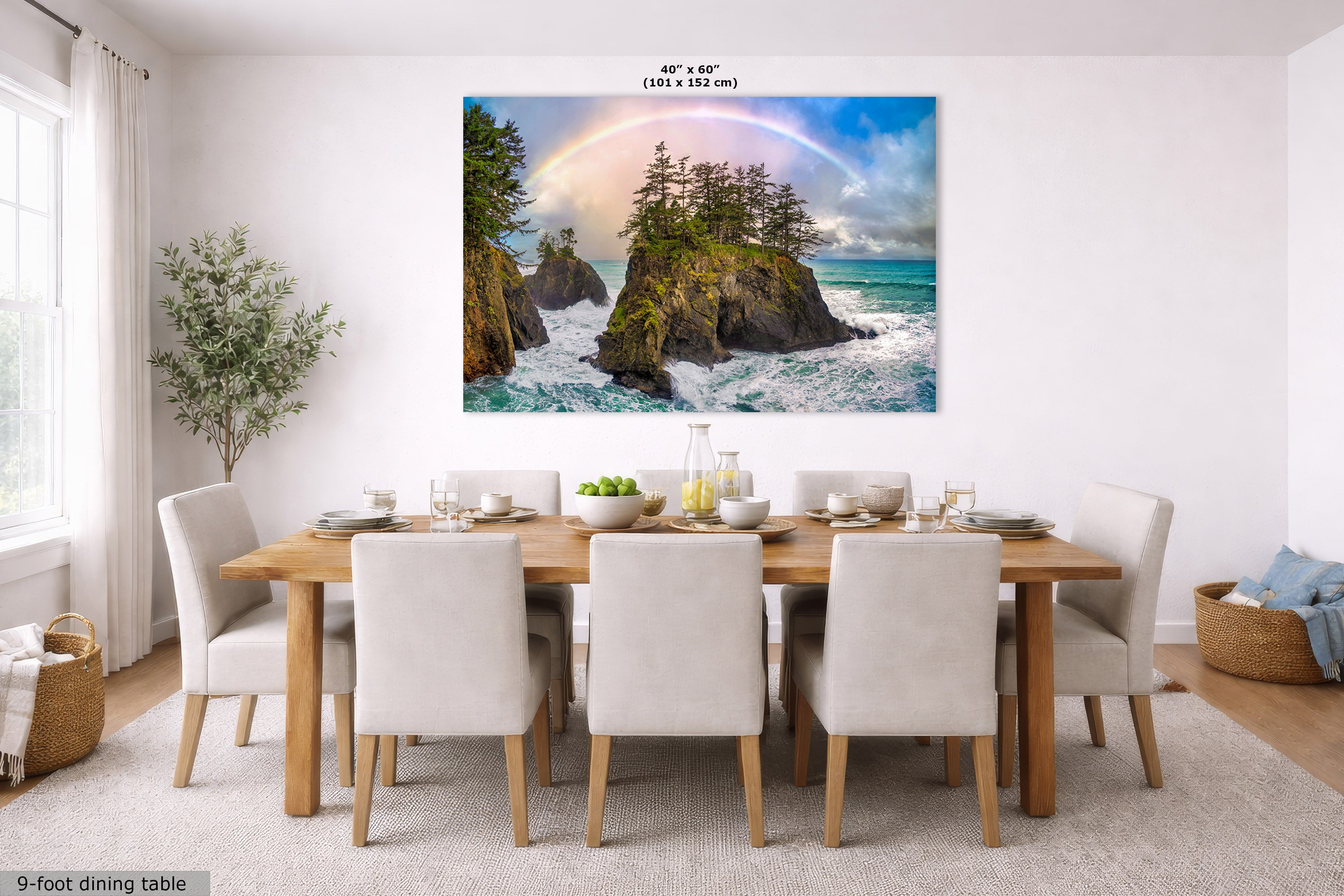 A large wall art print showing a rocky coastline with crashing waves, green trees, and a rainbow, displayed above a dining table in a bright modern room. The print includes size text reading 40" x 60" (101 x 152 cm).