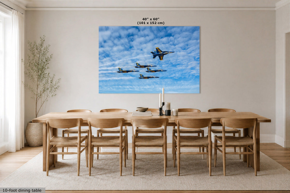 A large rectangular wall art print showing four blue-and-yellow jets flying through a bright blue sky with white clouds, displayed above a wooden dining table and chairs in a modern dining room. The print includes the text '40 in x 60 in (101 x 152 cm)' at the top.