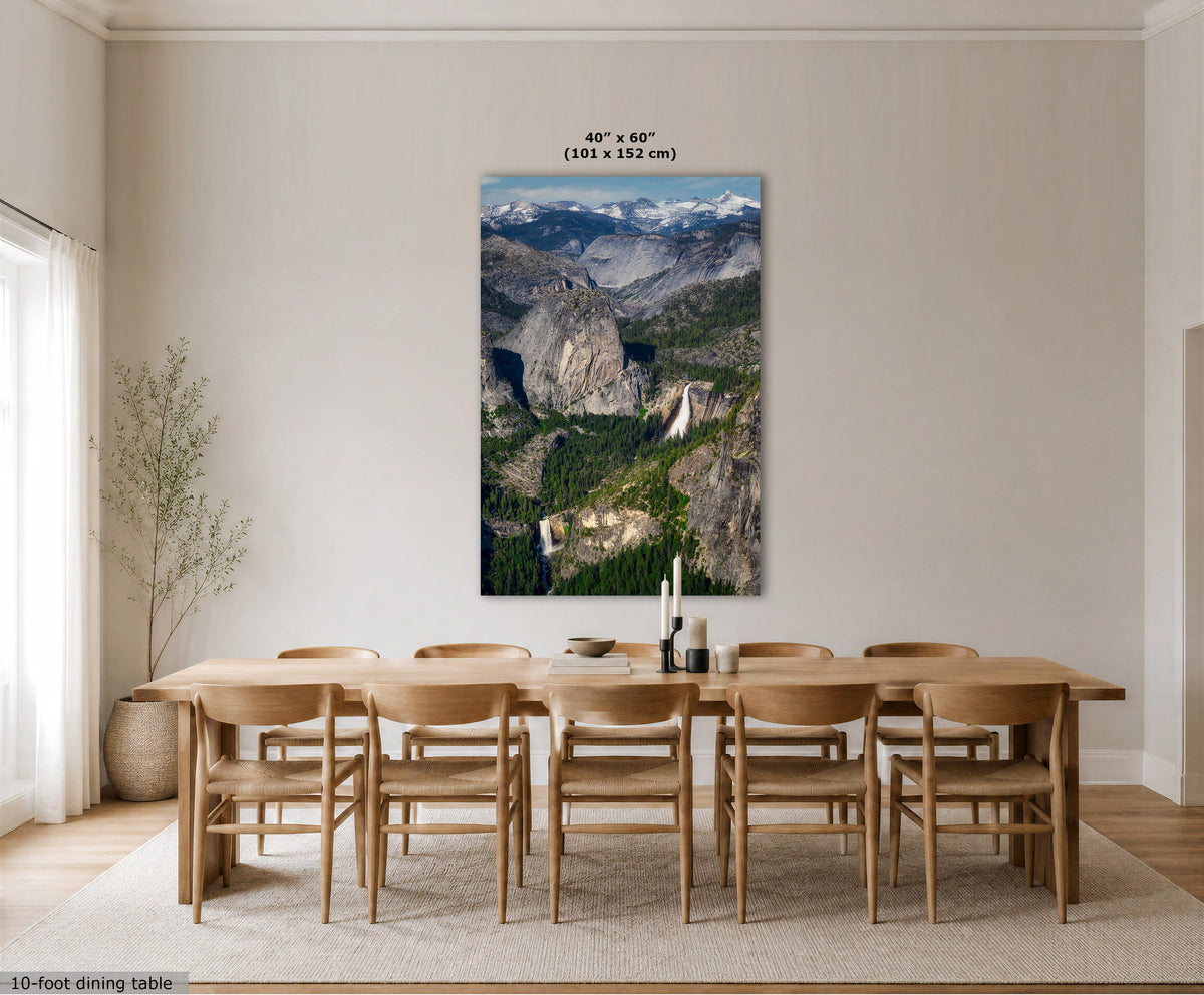 A large vertical wall art print showing a mountain valley landscape with waterfalls, displayed above a wooden dining table and chairs in a bright neutral dining room. Small text at the top indicates the print size as 40 x 60 inches, and a small text note at the bottom left says 10-foot dining table.