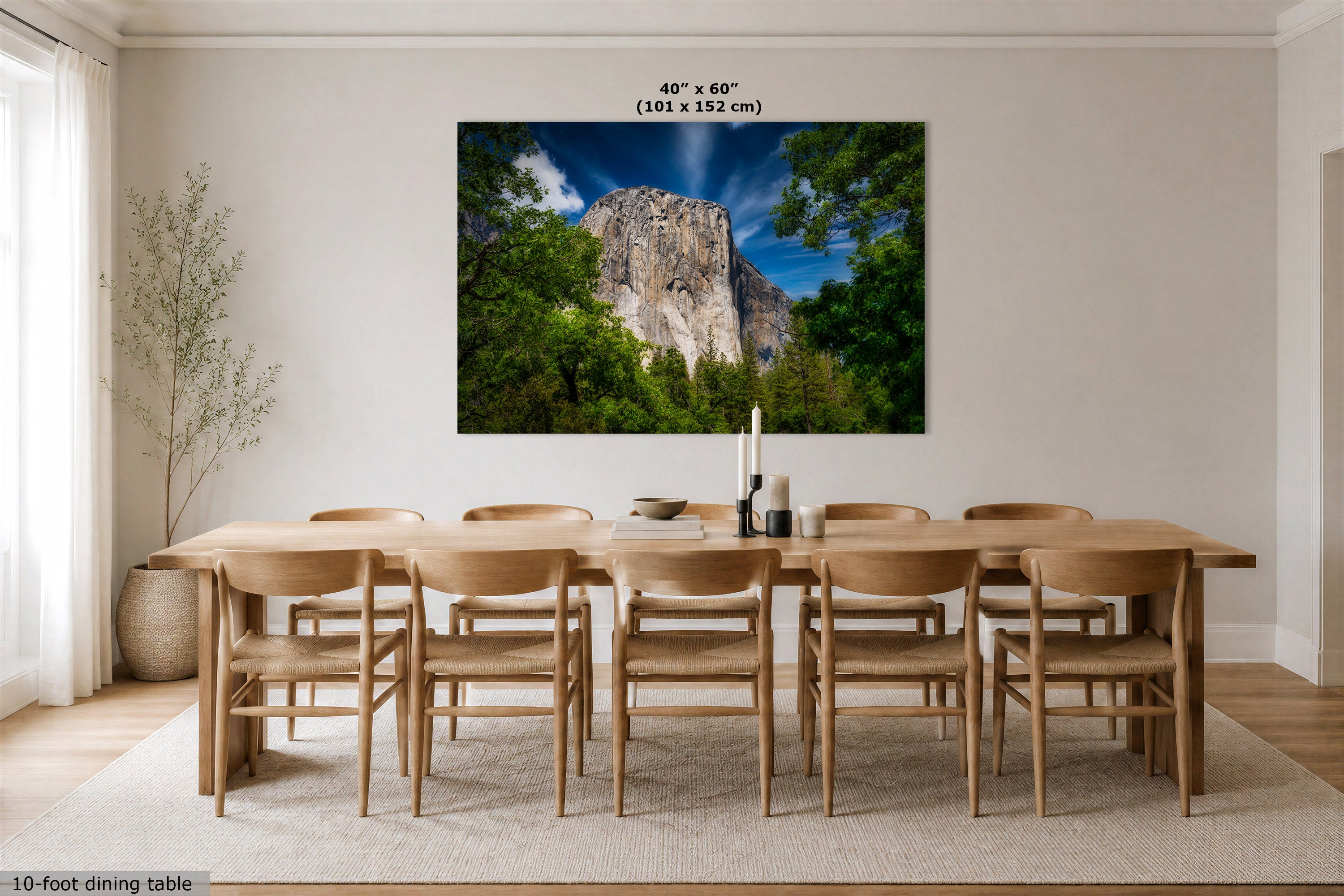 A large square wall art print showing a mountain landscape with green trees and a blue sky, displayed above a wooden dining table and chairs in a bright dining room. Text at the top reads 40 x 60 inches (101 x 152 cm), and text at the bottom left says 10-foot dining table.