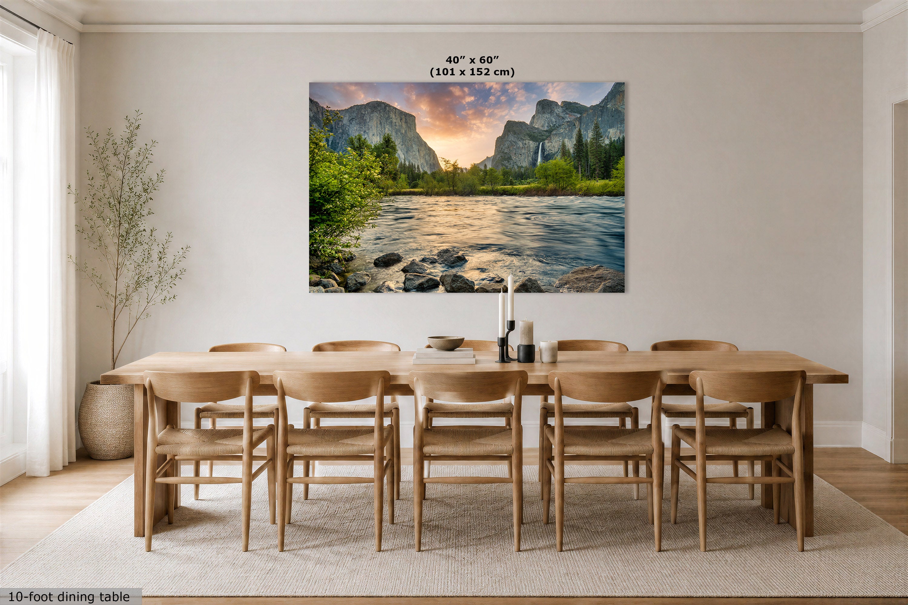 A large rectangular wall art print showing a mountain river landscape with a sunset sky, displayed above a wooden dining table and chairs in a bright dining room. The print includes size text reading 40" x 60" (101 x 152 cm).