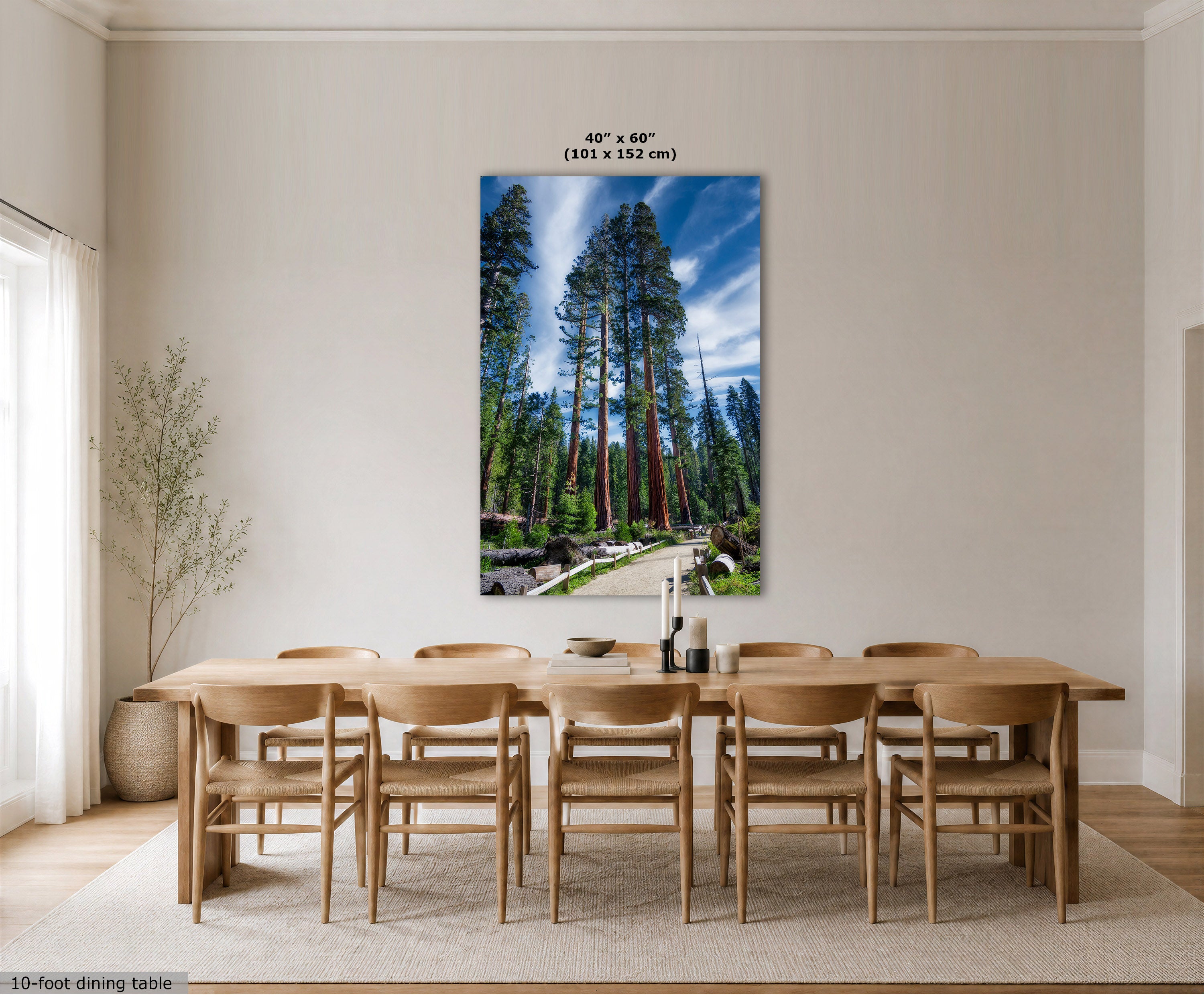 A large vertical wall art print showing a forest scene with tall trees and a blue sky, displayed above a wooden dining table and chairs in a bright neutral room. Text at the top indicates the print size as 40 x 60 inches (101 x 152 cm), and text at the bottom left says 10-foot dining table.