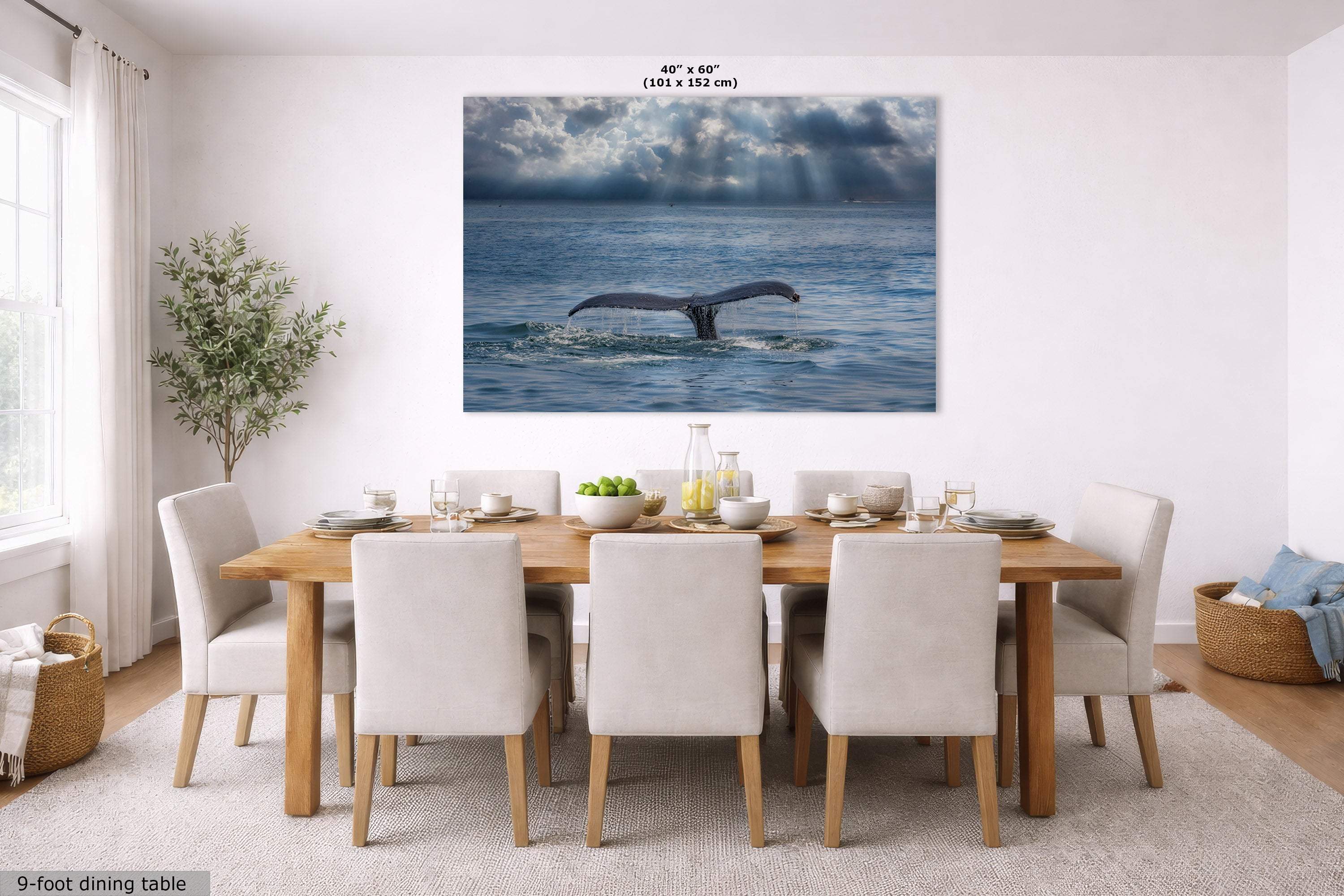 A large wall art print showing a whale tail in a blue ocean under dramatic clouds, displayed above a wooden dining table with white chairs in a bright dining room. The print includes size text at the top and a small label at bottom left.