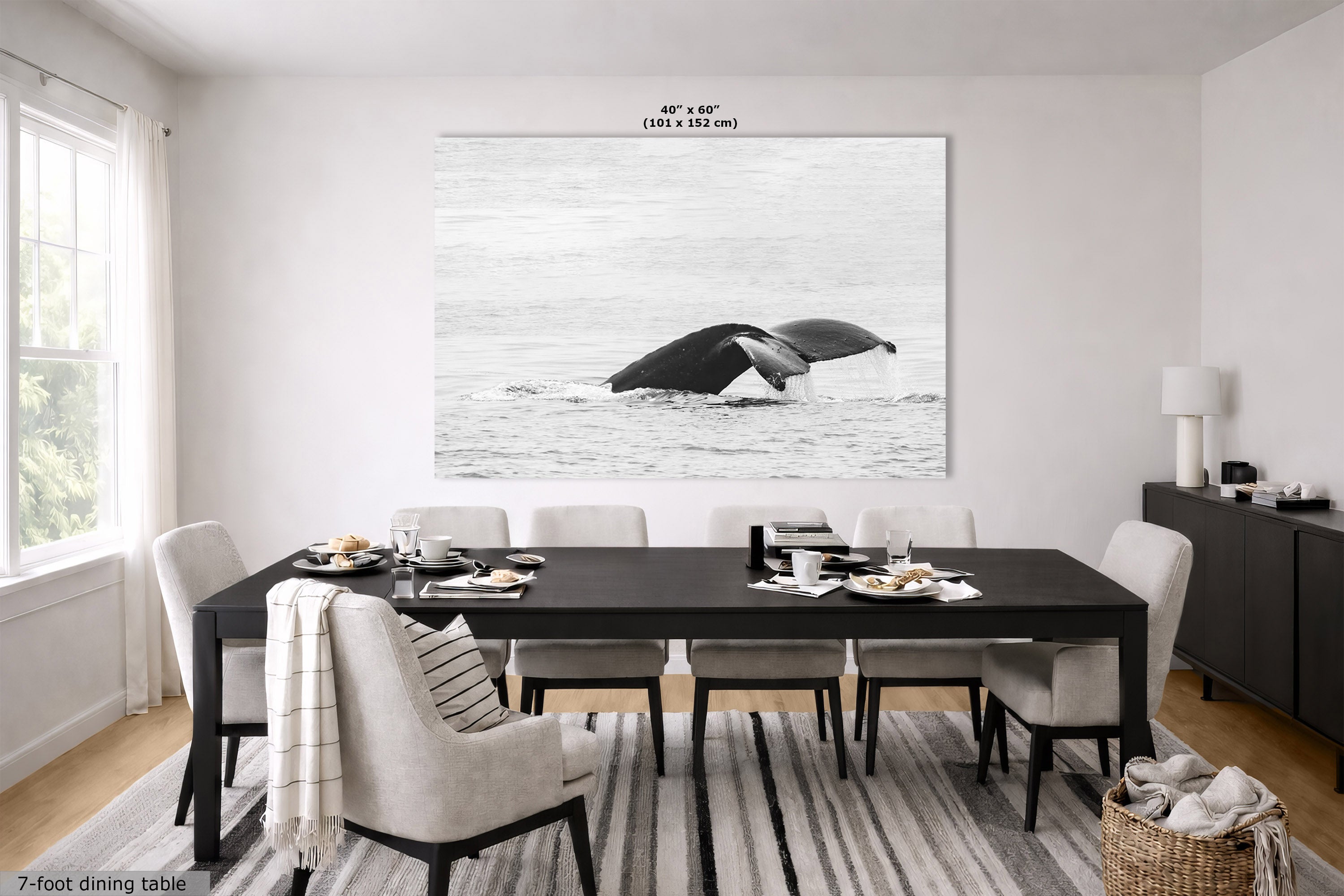 A large black-and-white humpback whale fluke wall art print displayed above a dining table in a modern dining room. The print shows a whale breaching in the ocean, with dimensions '40" x 60" (101 x 152 in)' printed above the artwork.