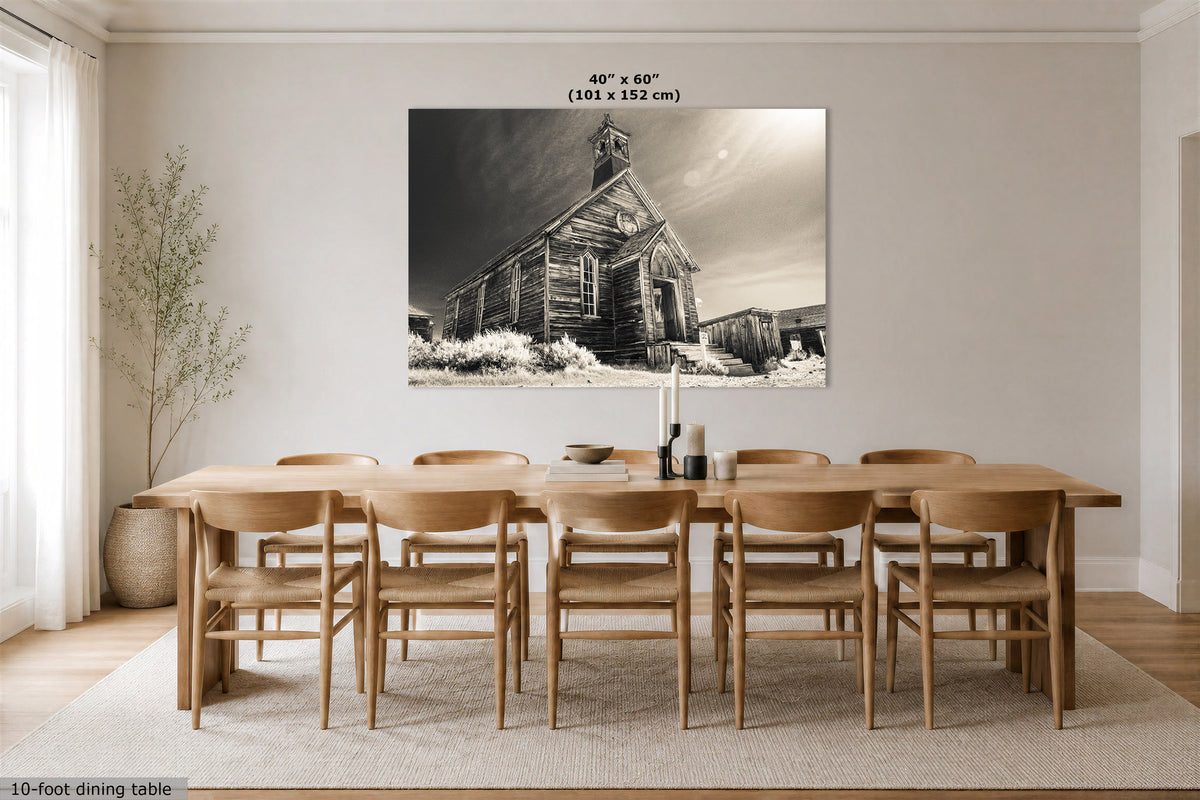 A 40" x 60" black and white canvas print of an old wooden church, displayed on a dining room wall above a wooden dining table and chairs.