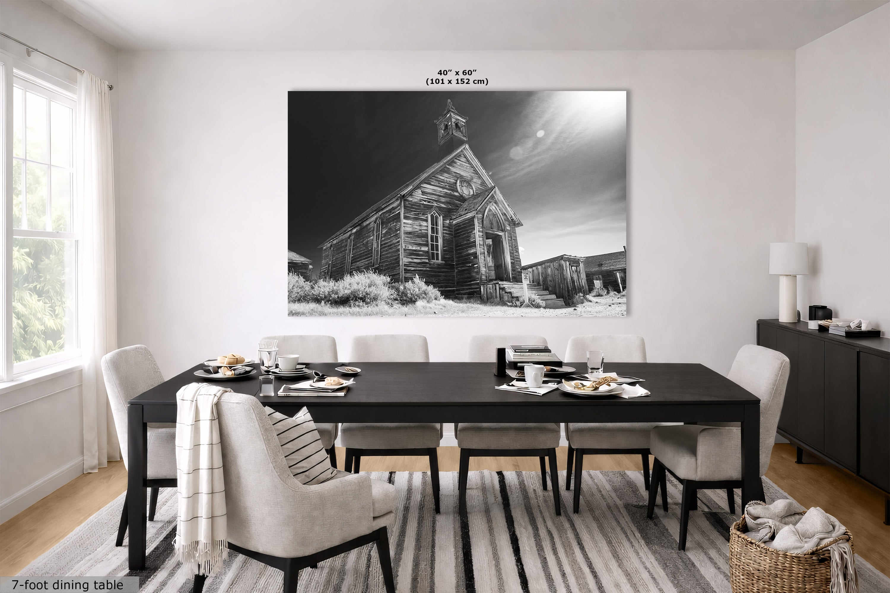 A large black and white wall art print depicting an old wooden church under a cloudy night sky, displayed in a modern dining room setting above a dark wood table and chairs. The dimensions '40" x 60"' are printed above the artwork.