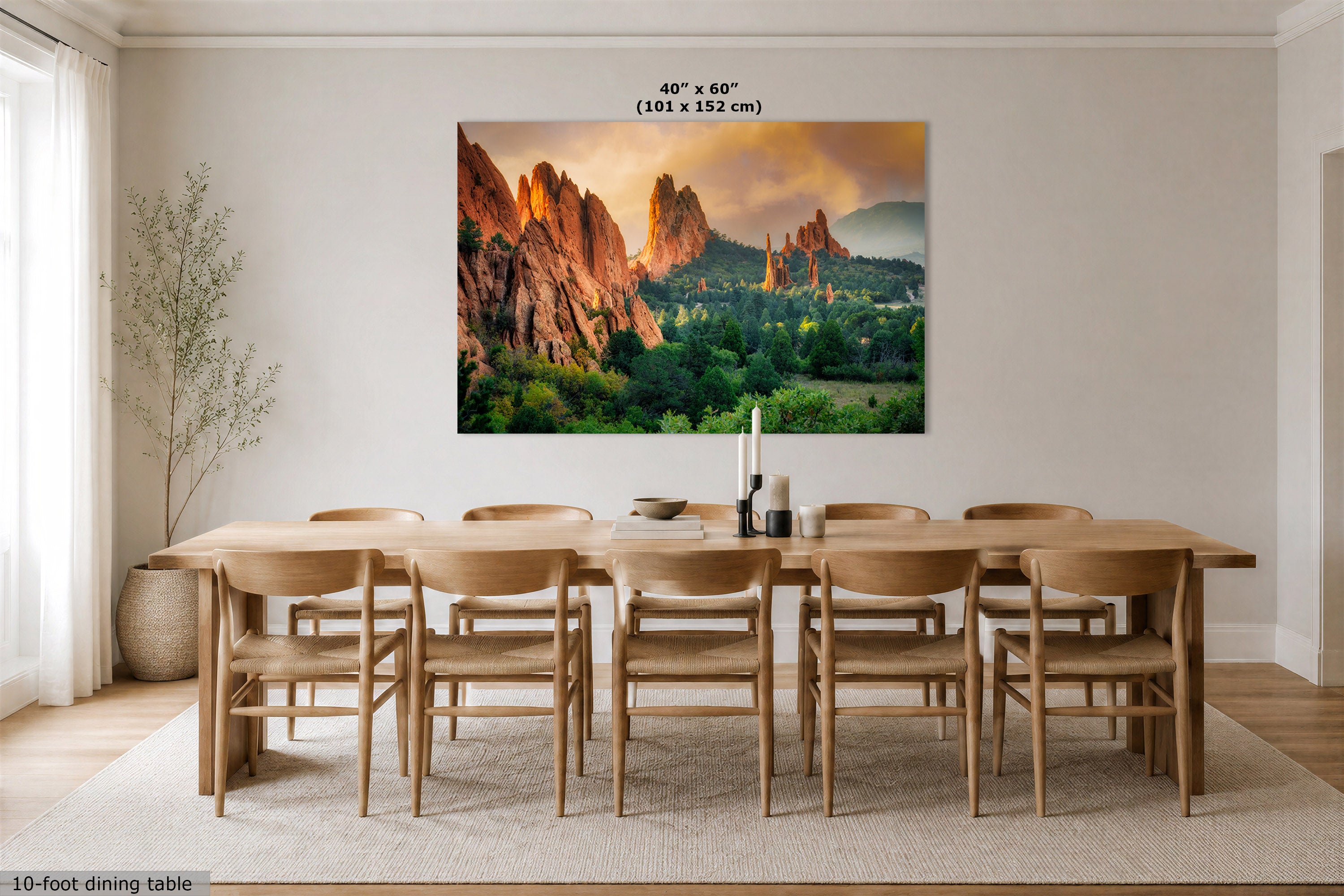 A large rectangular wall art print showing a colorful desert rock landscape at sunset, displayed above a wooden dining table and chairs in a bright modern dining room. Text at the top reads 40 in x 60 in (101 x 152 cm), and a small note at bottom left says 10-foot dining table.