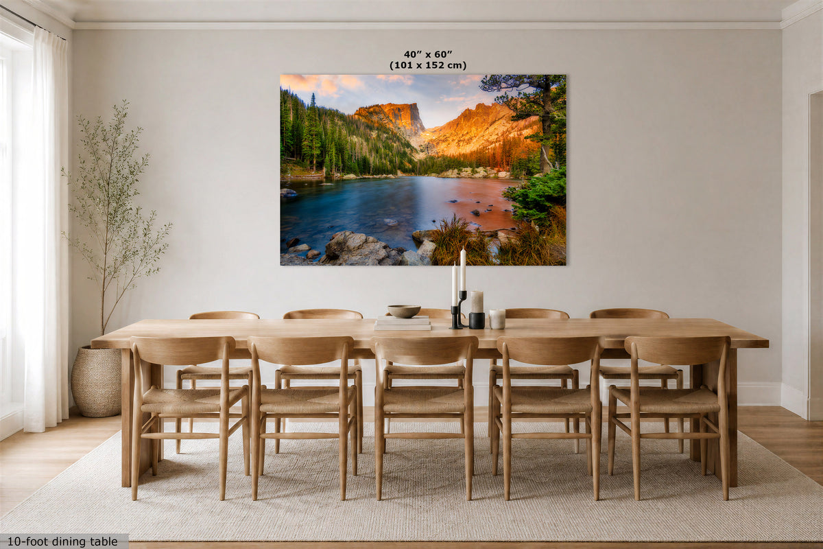 A large wall art print showing a colorful mountain lake landscape hangs above a wooden dining table and chairs in a bright dining room. Text at the top of the print reads 40" x 60" (101 x 152 cm), and small text at the bottom left says 10-foot dining table.