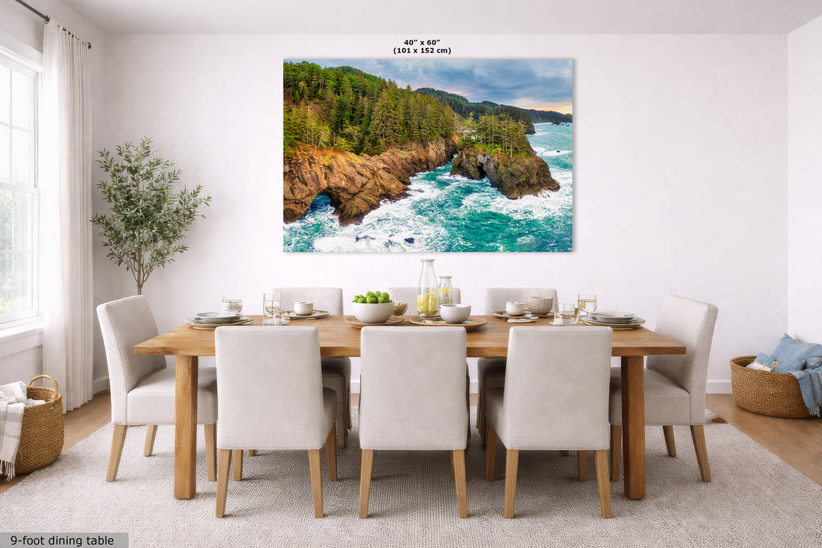 A large square wall art print showing a rocky coastline with turquoise ocean waves and green forest, displayed above a dining table in a bright modern room. Small text at the top reads 40" x 60".