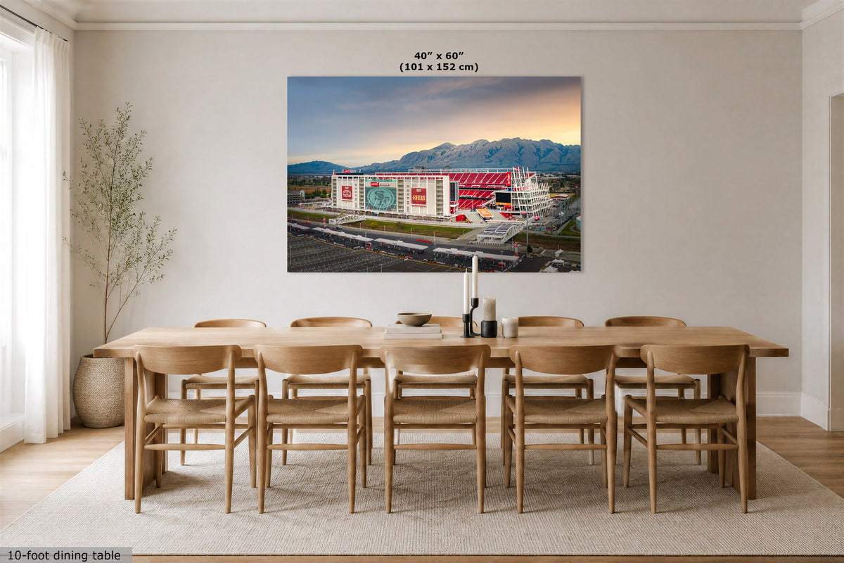 A 40" x 60" Levi's Stadium sunrise wall art print depicting a stadium under a sunset sky, displayed in a modern dining room setting above a wooden dining table and chairs.