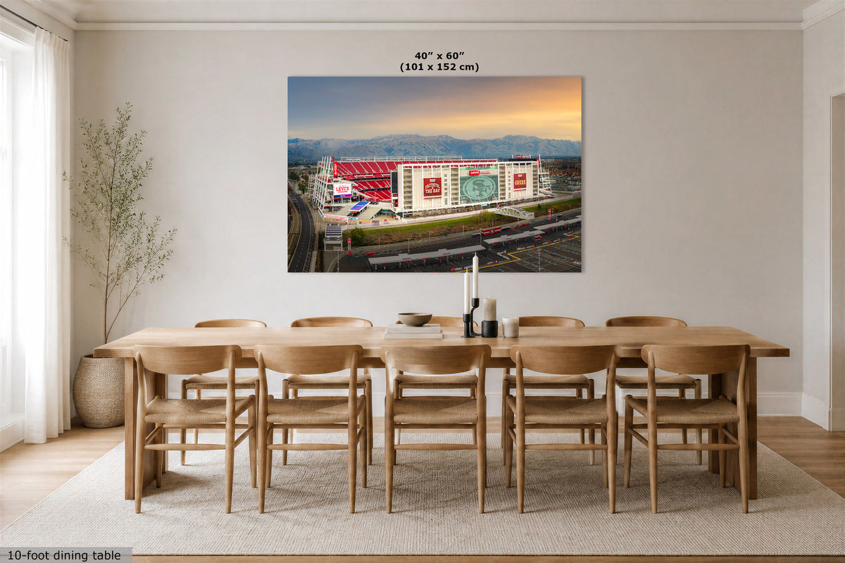 A large wall art print showing an aerial view of a stadium at sunrise, displayed above a wooden dining table in a modern dining room. The print includes the text '40" x 60" (101 x 152 cm)' at the top.