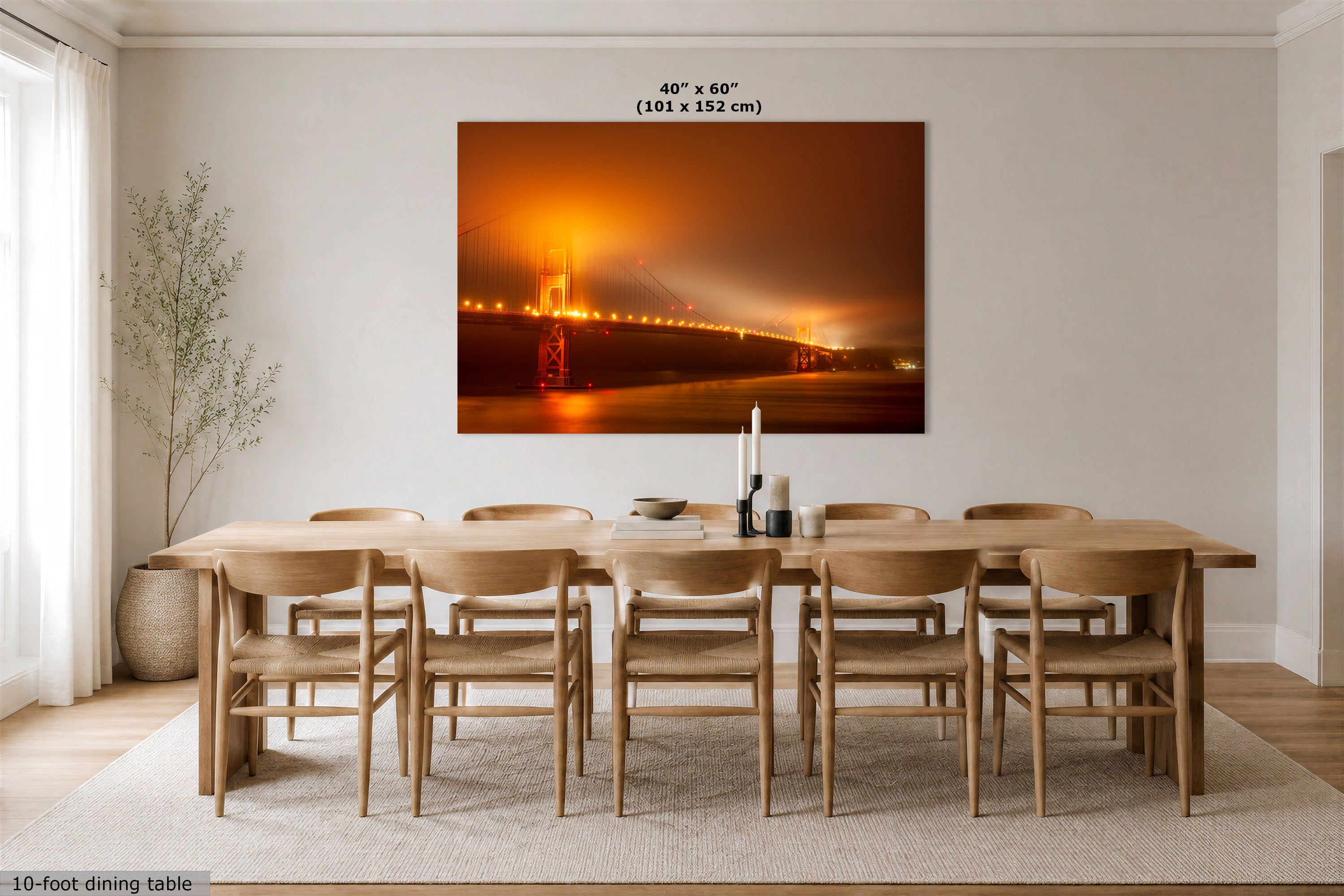 A large rectangular wall art print of San Francisco, showing a glowing orange Golden Gate Bridge shrowded in fog at night, displayed above a wooden dining table and chairs in a bright modern dining room. Text at the top of the print reads 40 x 60 inches (101 x 152 cm).