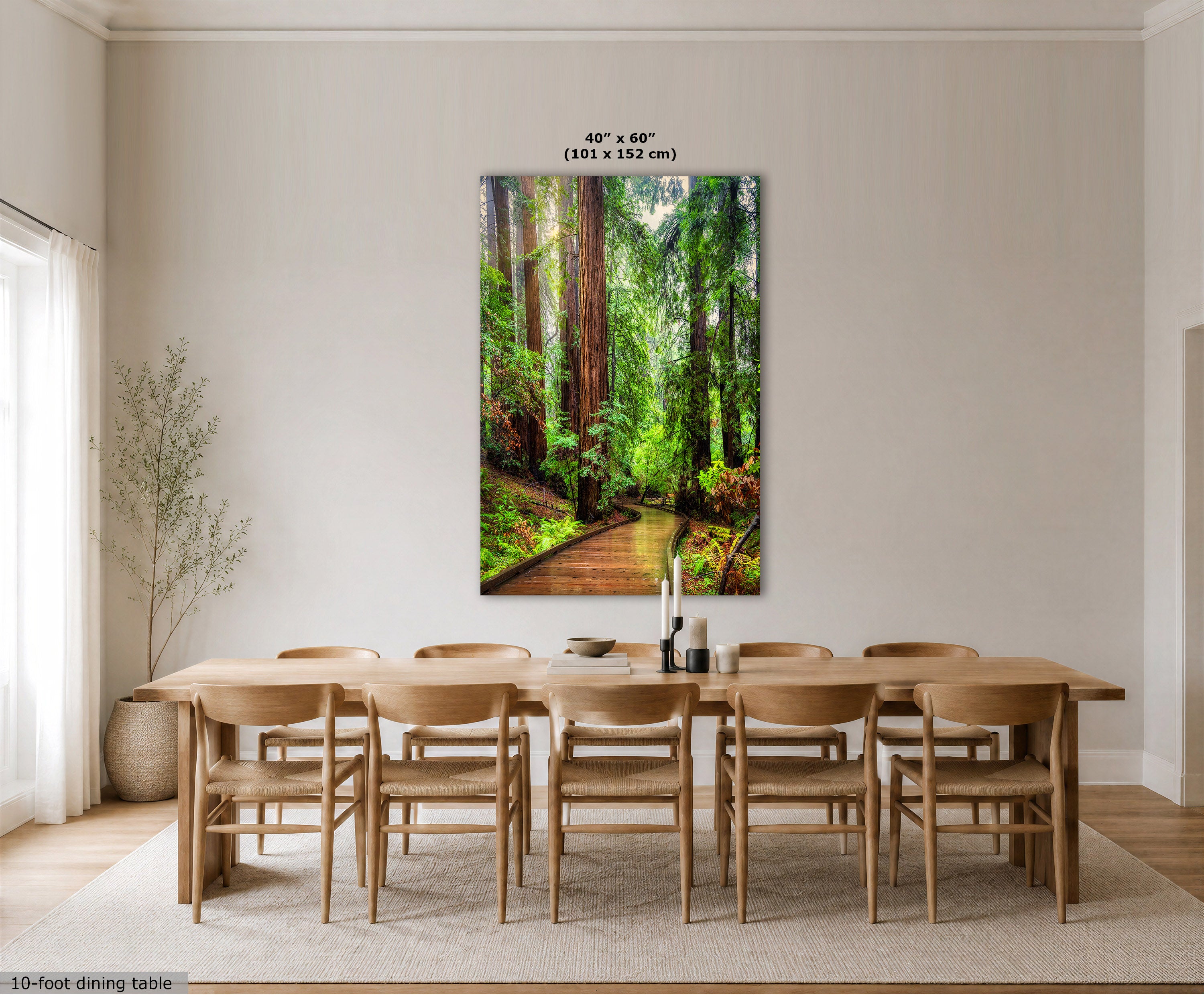 A vertical wall art print depicting a lush green forest path with tall trees, displayed above a wooden dining table and chairs in a bright, modern dining room. The print includes size text at the top and a small text label in the bottom left corner.