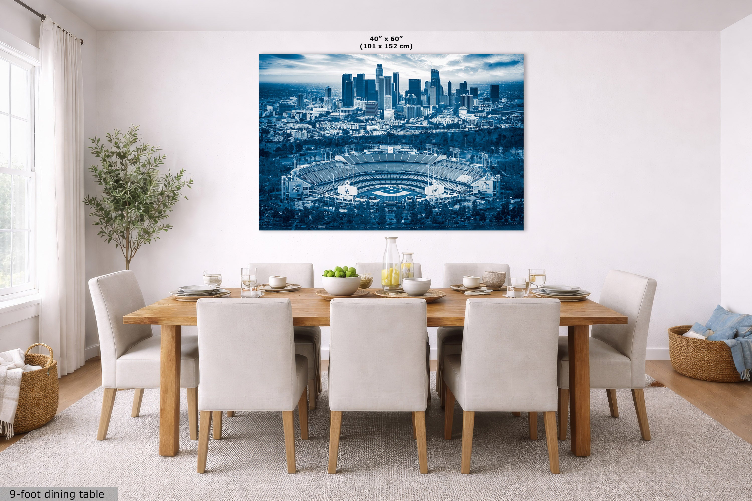A large rectangular wall art print showing a blue-toned city skyline and stadium, displayed above a dining table in a bright modern room. Small text at the top reads 40" x 60" and text at the bottom left reads 9-foot dining table.
