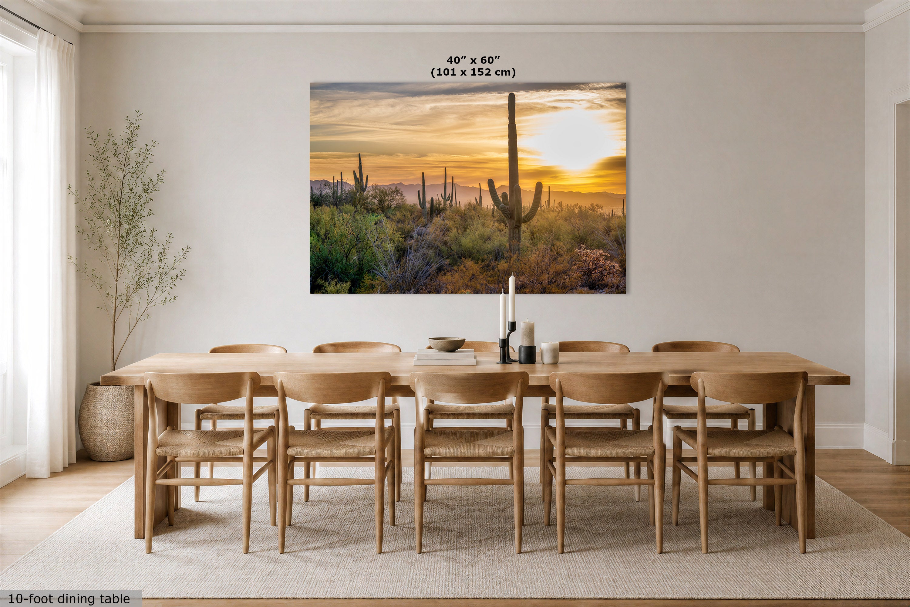A large wall art print showing a desert sunset with cacti is displayed above a wooden dining table and chairs in a bright dining room. The print includes size text reading 40" x 60" (101 x 152 cm) at the top.