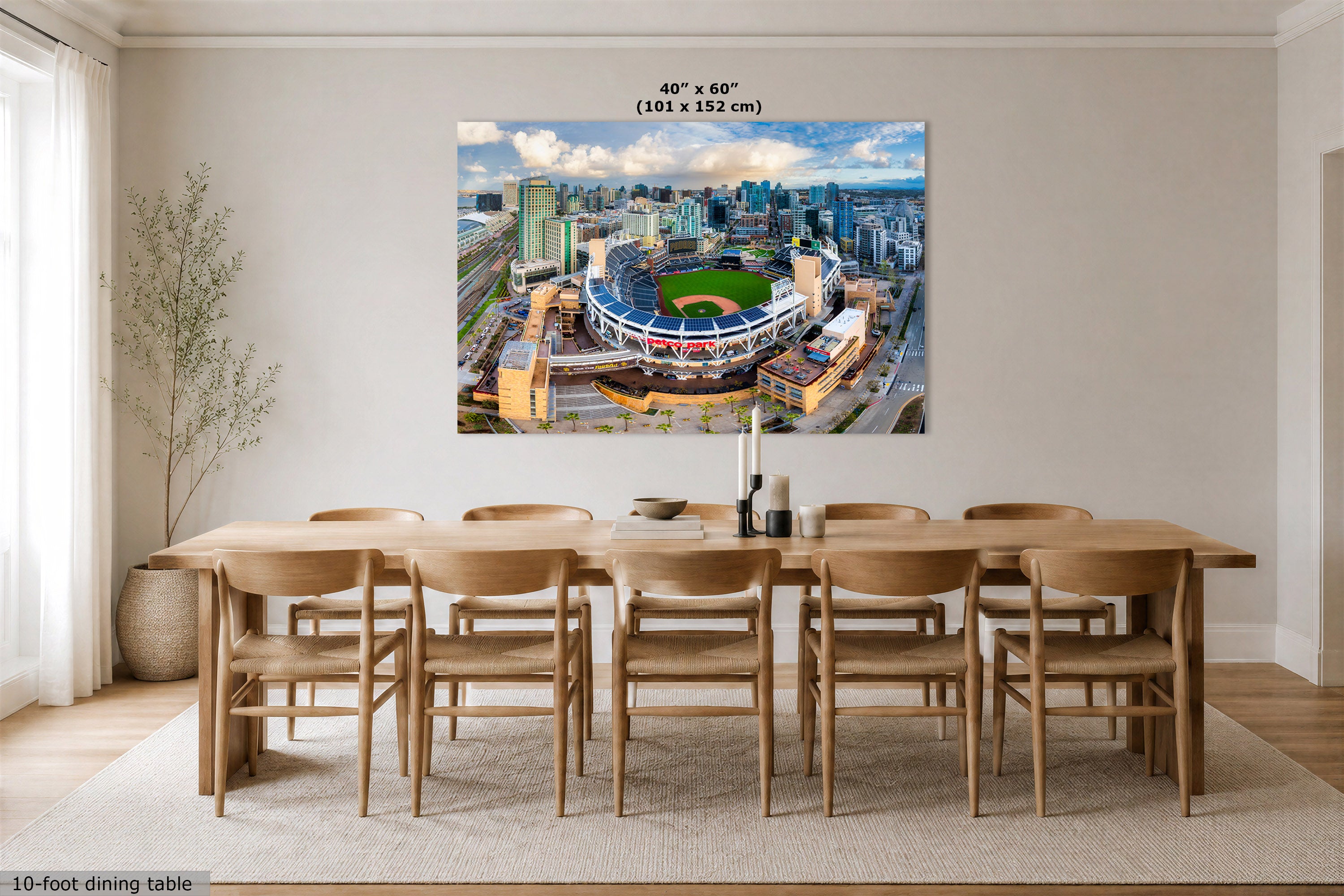 A large San Diego Padres skyline art print depicting an aerial view of a baseball stadium and the surrounding city skyline, displayed above a wooden dining table in a bright, modern dining room. The print includes size text at the top reading 40" x 60" (102 x 152 cm).