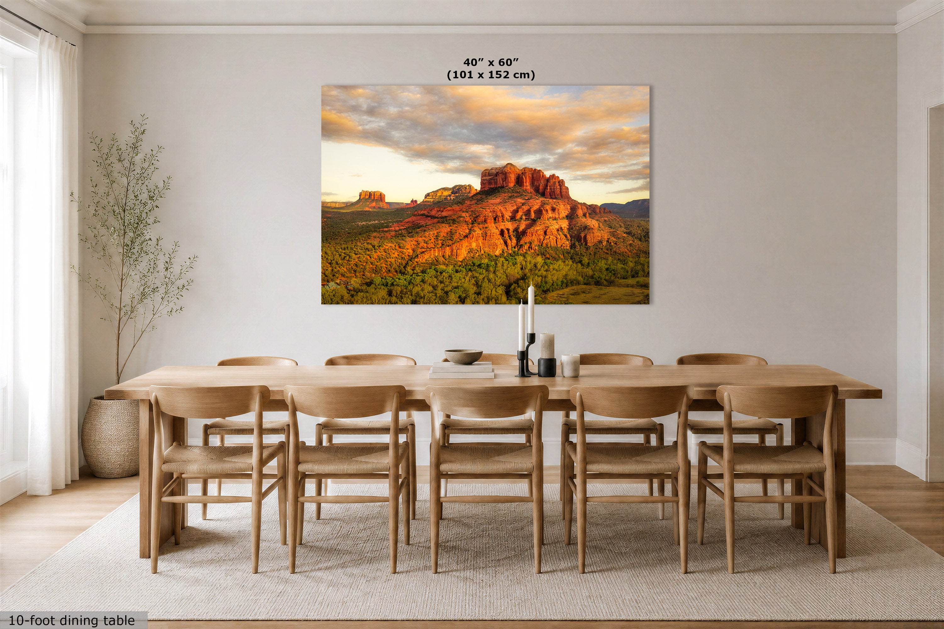 A large rectangular wall art print showing a desert rock landscape at sunset hangs above a 10-foot dining table and chairs in a bright, modern dining room. The print includes the text '40" x 60" (101 x 152 cm)' at the top.