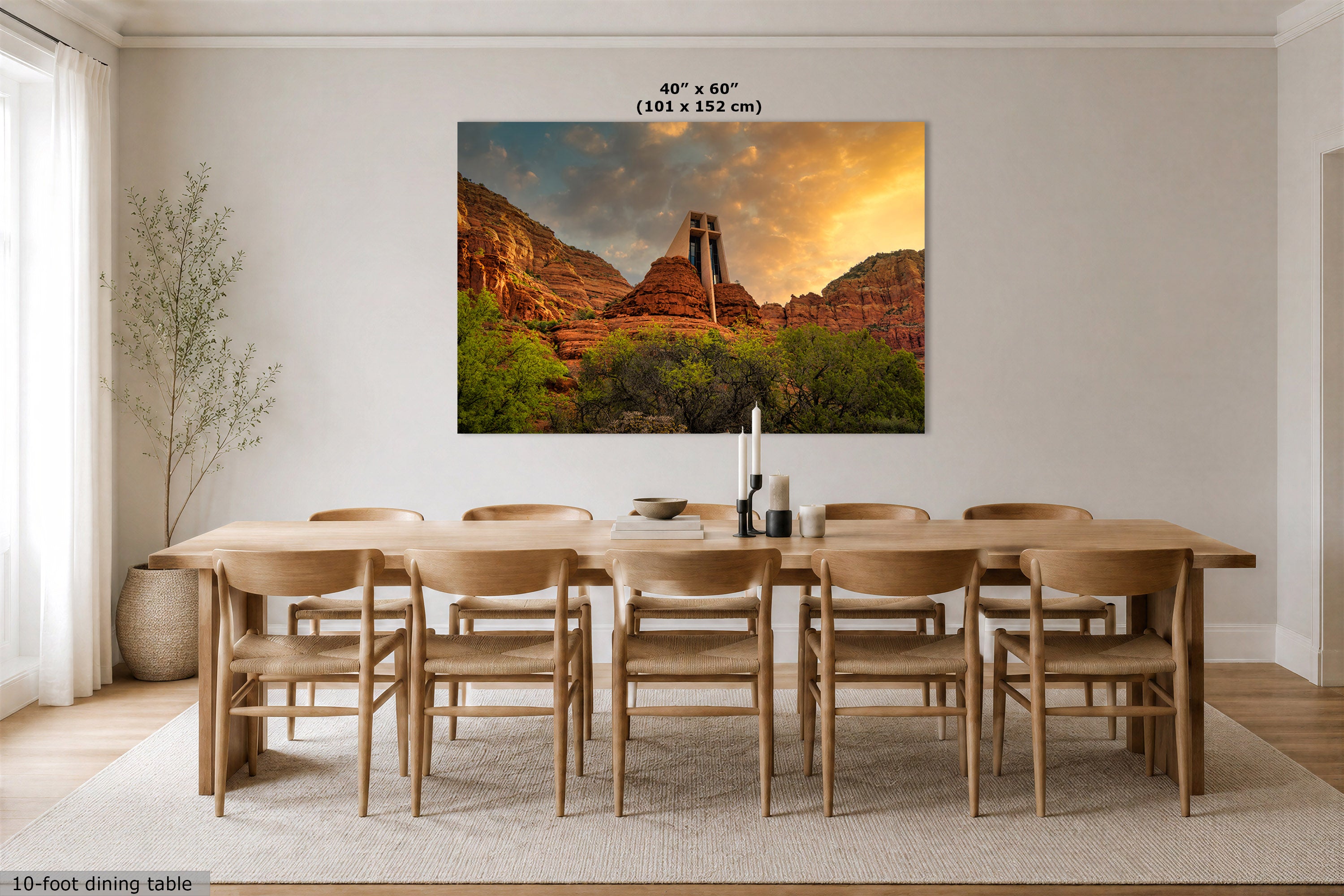 A 40" x 60" canvas print of a Sedona desert landscape with a sunset is displayed on a dining room wall above a 10-foot wooden dining table and chairs. The room has beige walls, light wood flooring, and a neutral rug.