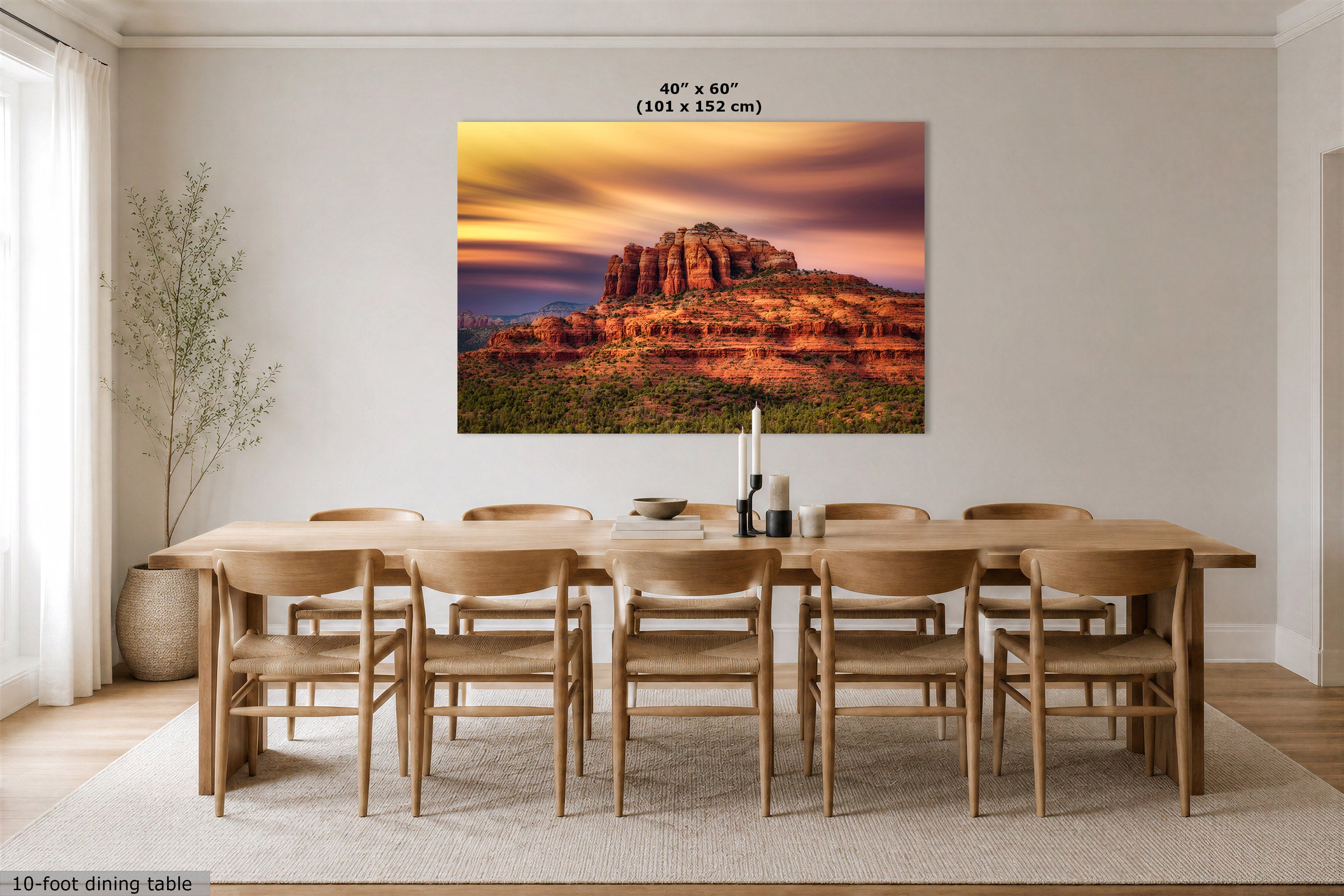 A large rectangular wall art print showing a desert rock landscape at sunset, displayed above a wooden dining table and chairs in a bright neutral dining room. Text at the top reads 40" x 60" (101 x 152 cm), and a small note at bottom left says 10-foot dining table.