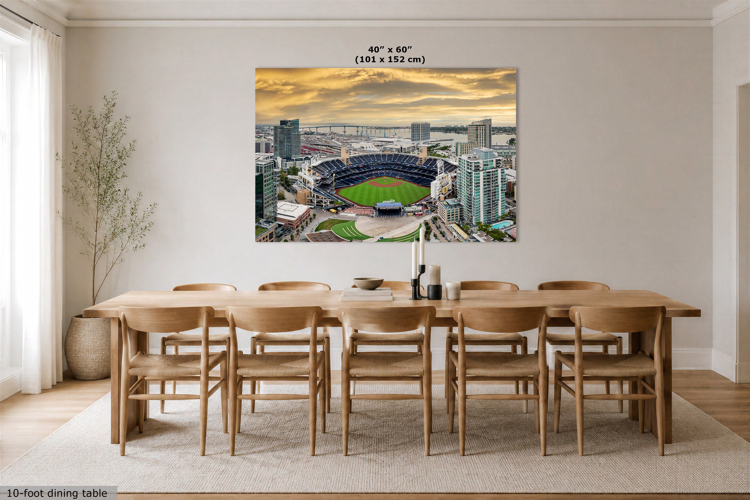 A large rectangular wall art print showing an aerial stadium scene at sunset, displayed above a wooden dining table and chairs in a modern dining room. The print includes size text at the top reading 40" x 60" (101 x 152 cm).