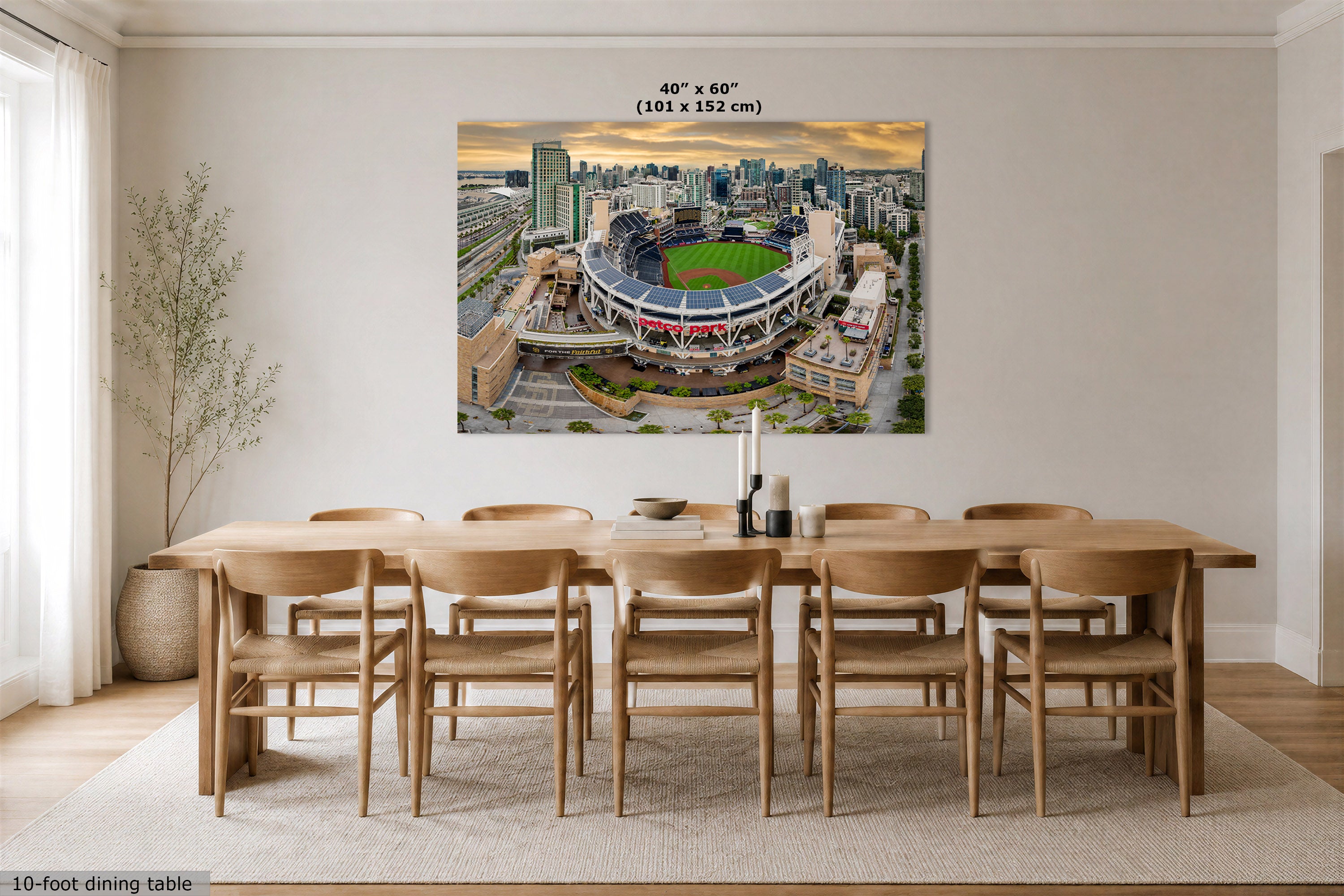 A large rectangular wall art print showing an aerial stadium scene, displayed above a wooden dining table and chairs in a bright modern dining room. The print includes size text at the top reading 40" x 60" (101 x 152 cm).