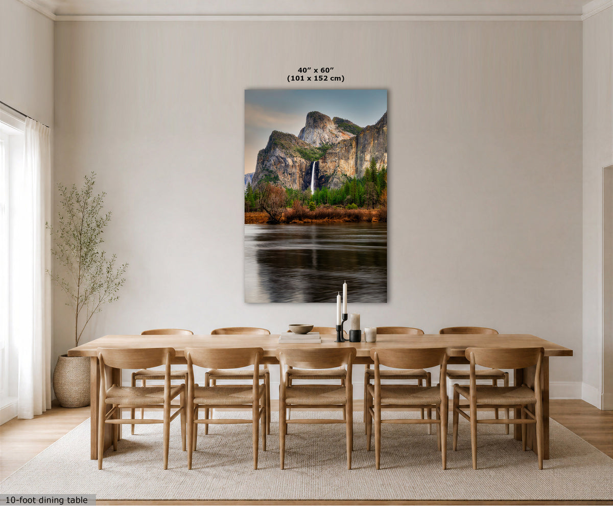 A large vertical wall art print depicting a mountain landscape with a waterfall and reflective water, displayed above a wooden dining table and chairs in a bright neutral dining room. Text at the top reads 40" x 60" (101 x 152 cm), and a small note at bottom left says 10-foot dining table.