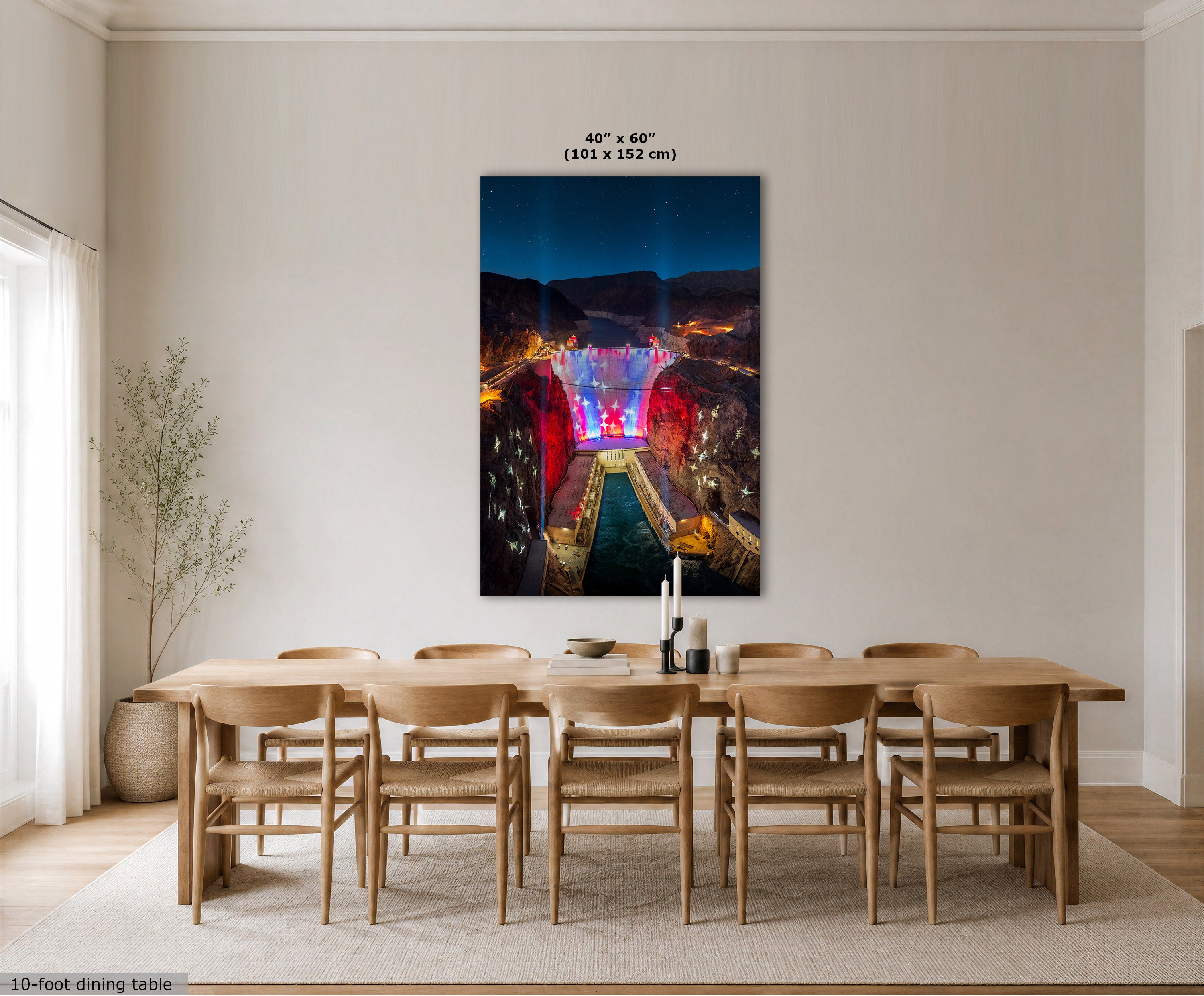 A large vertical wall art print showing a colorful night aerial view of a canyon or stadium scene, displayed above a light wood dining table and chairs in a bright neutral dining room. Text at the top reads 40" x 60" (101 x 152 cm), and a small label at bottom left says 10-foot dining table.
