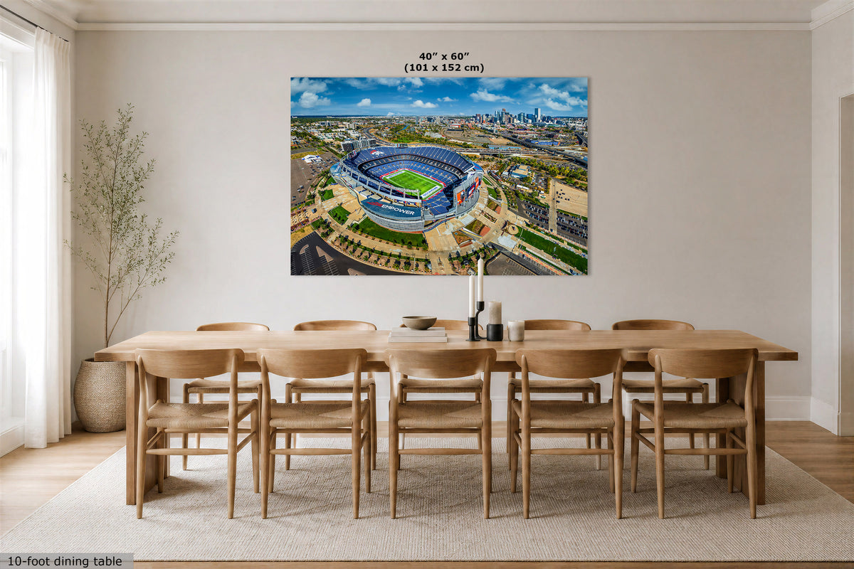 A large wall art print showing an aerial stadium scene, displayed above a wooden dining table in a bright modern dining room. The print includes size text at the top reading 40" x 60" (101 x 152 cm).