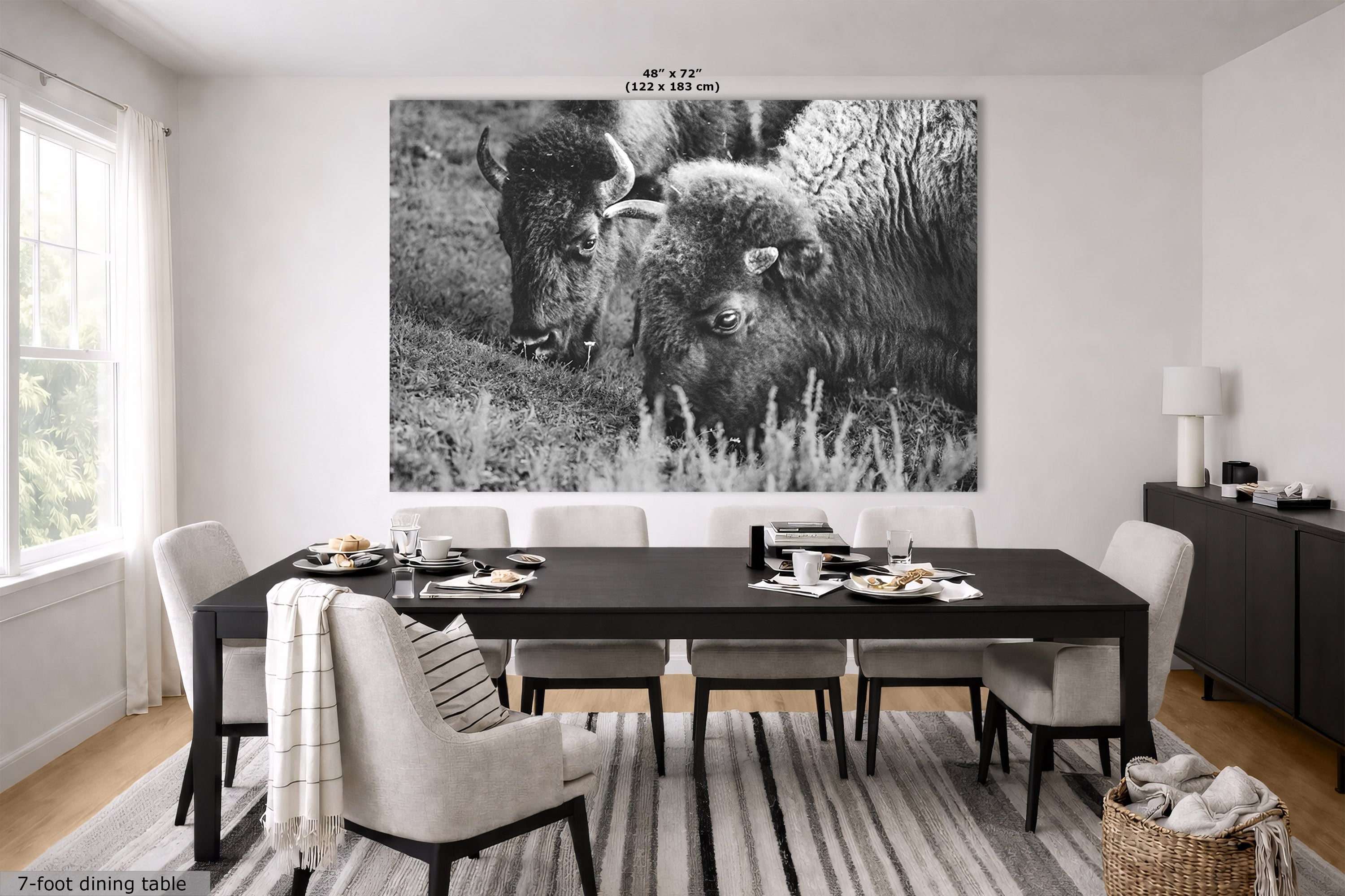 A large black and white wall art print depicting two bison in a grassy field, displayed above a dining table in a modern dining room setting.